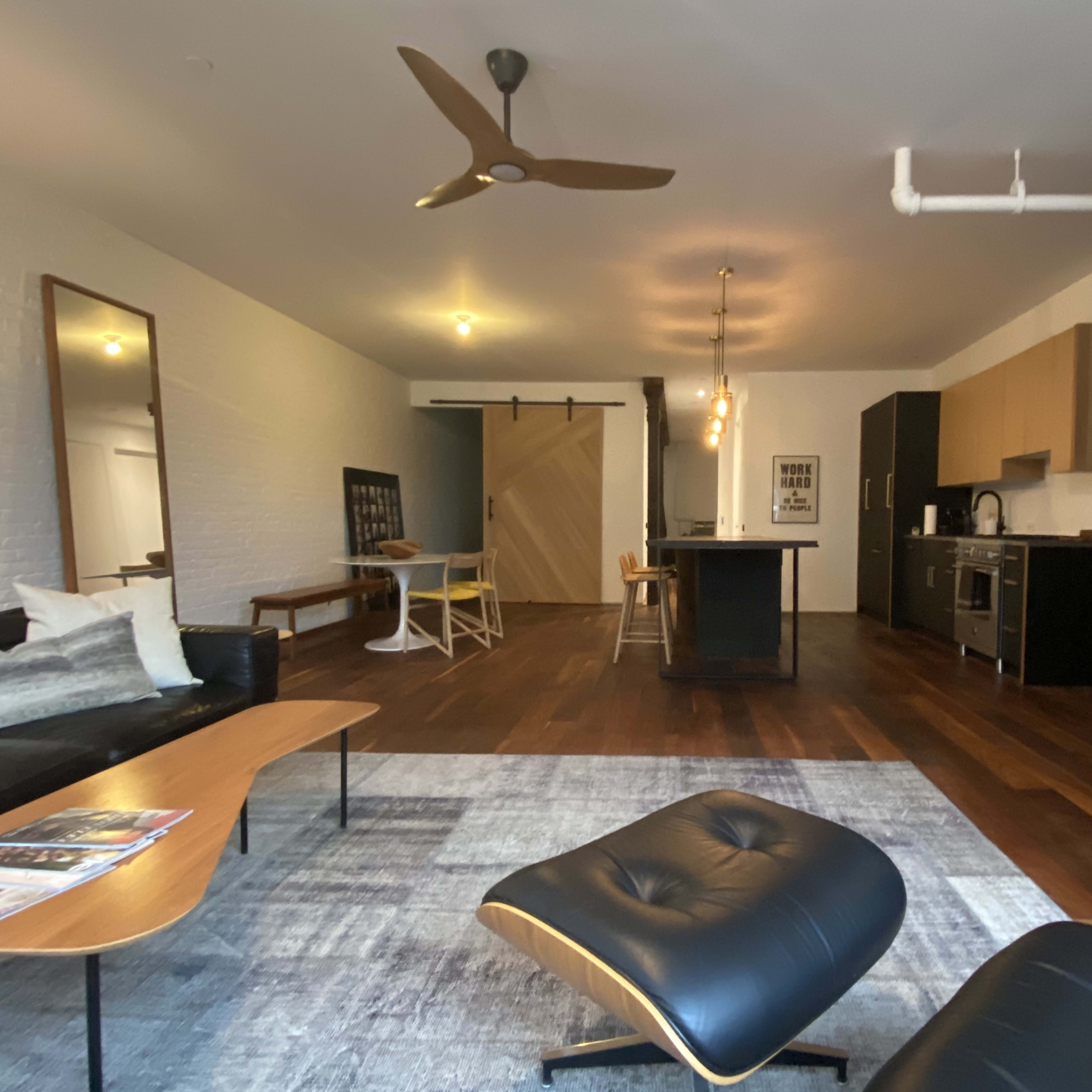 A modern living space featuring hardwood floors, a sectional sofa, a dining area, and a kitchen with wooden cabinetry.