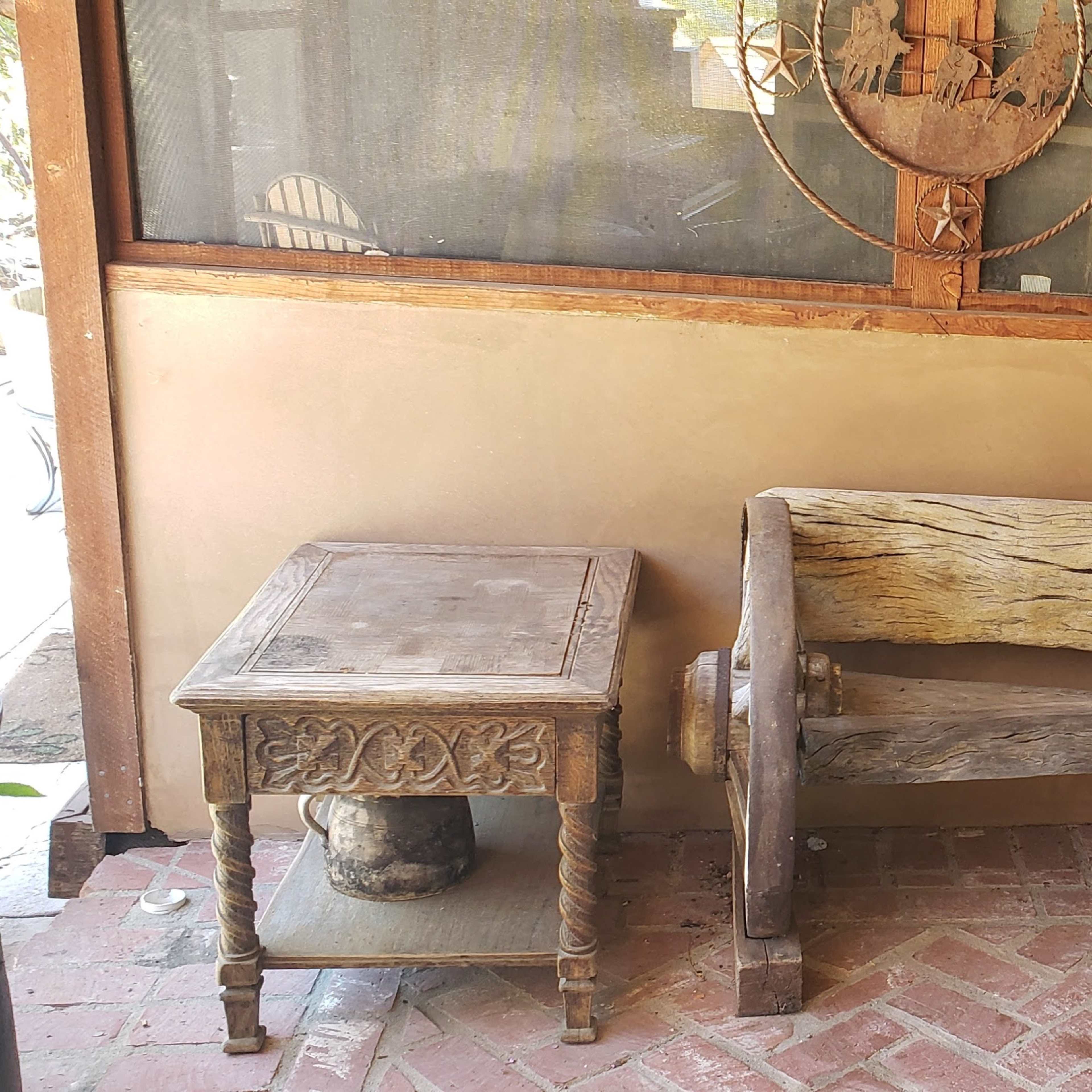 A rustic wooden bench made from a large wheel and a small side table, set against a wall with a window and various items in the background.