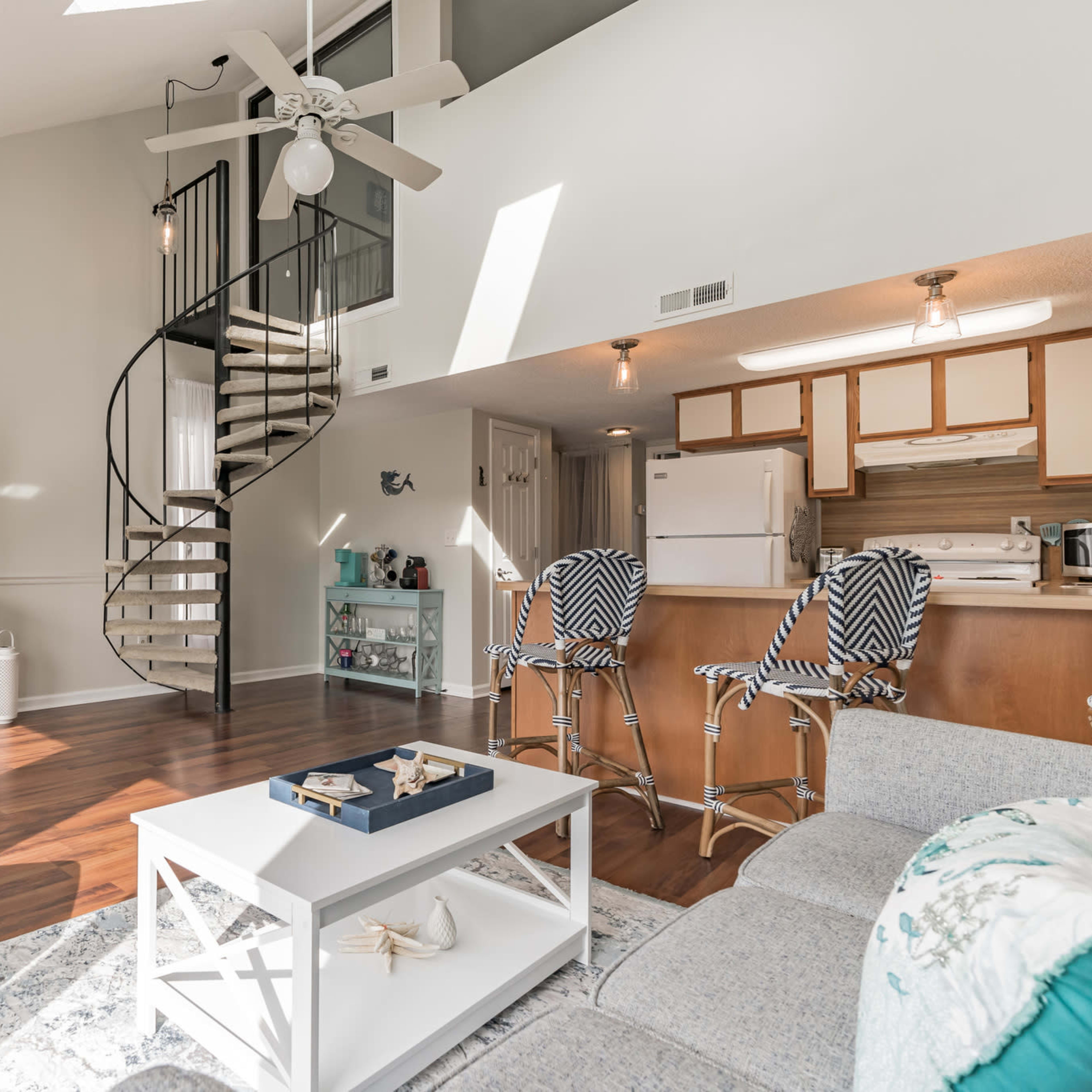A bright living room with a spiral staircase, a television, and a kitchen area in an open layout.