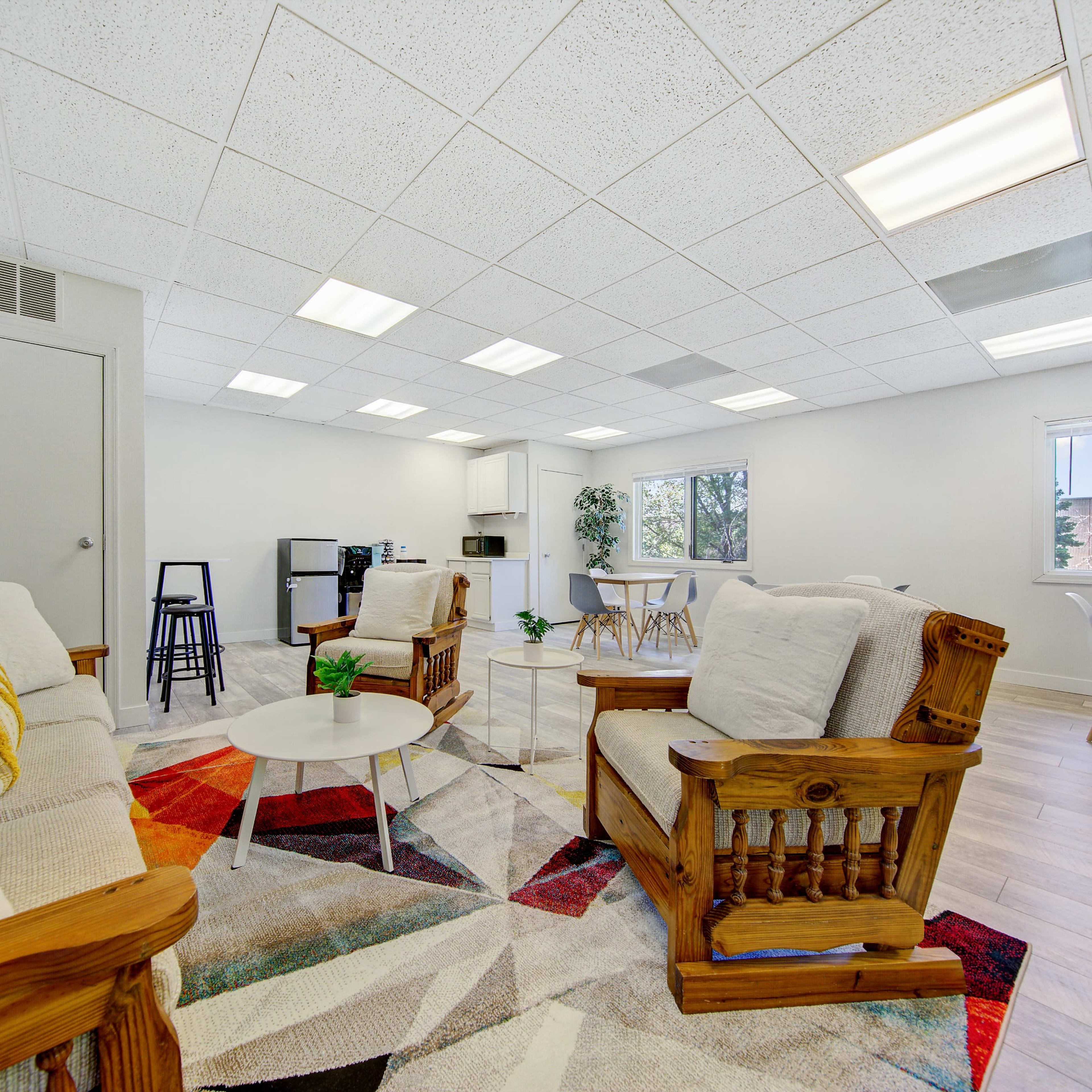 A modern, open-plan communal space with comfortable seating, a kitchenette, dining area, and large windows allowing natural light.