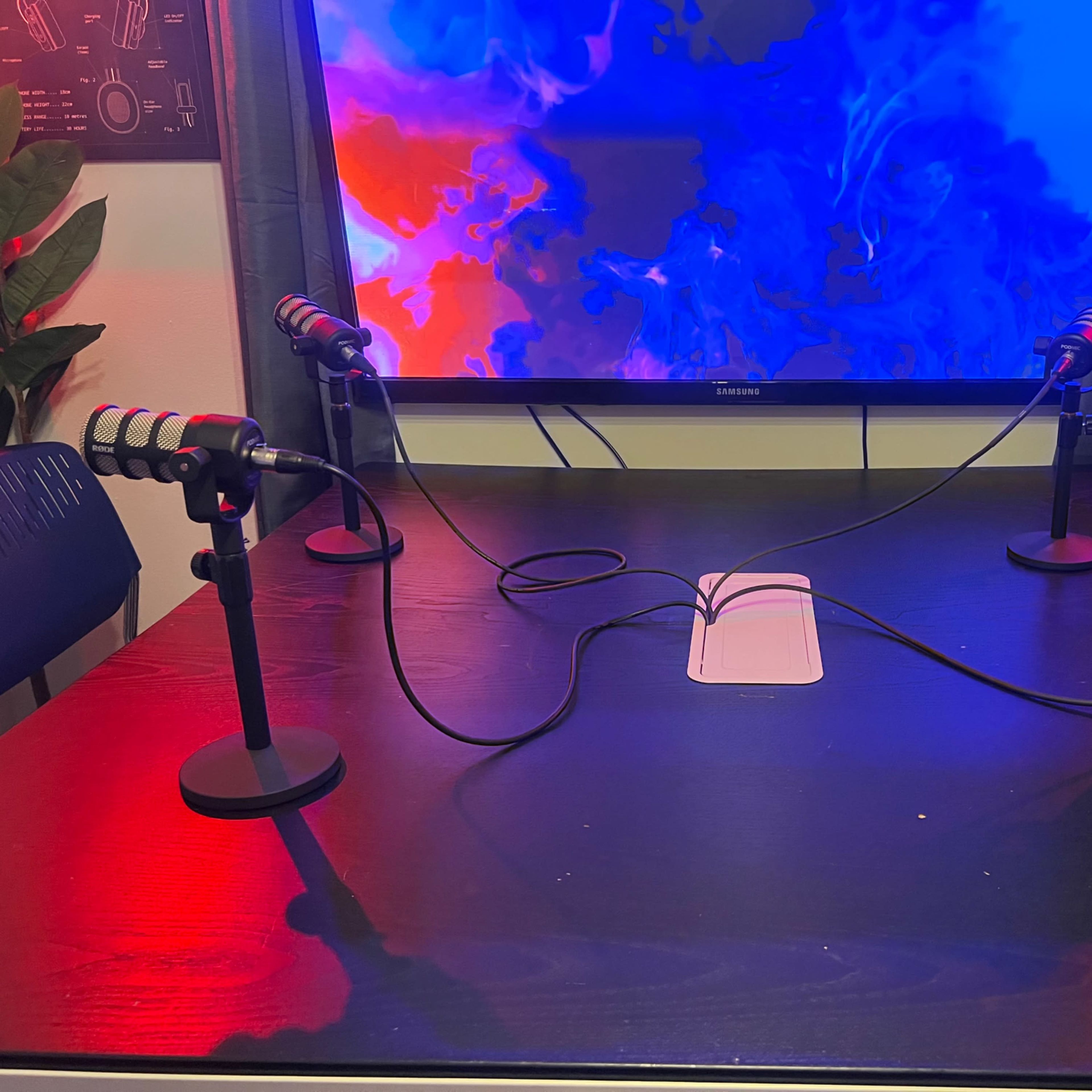 A wooden table with four microphones attached to stands, connected by cables, sits in front of a colorful backdrop on a television screen.