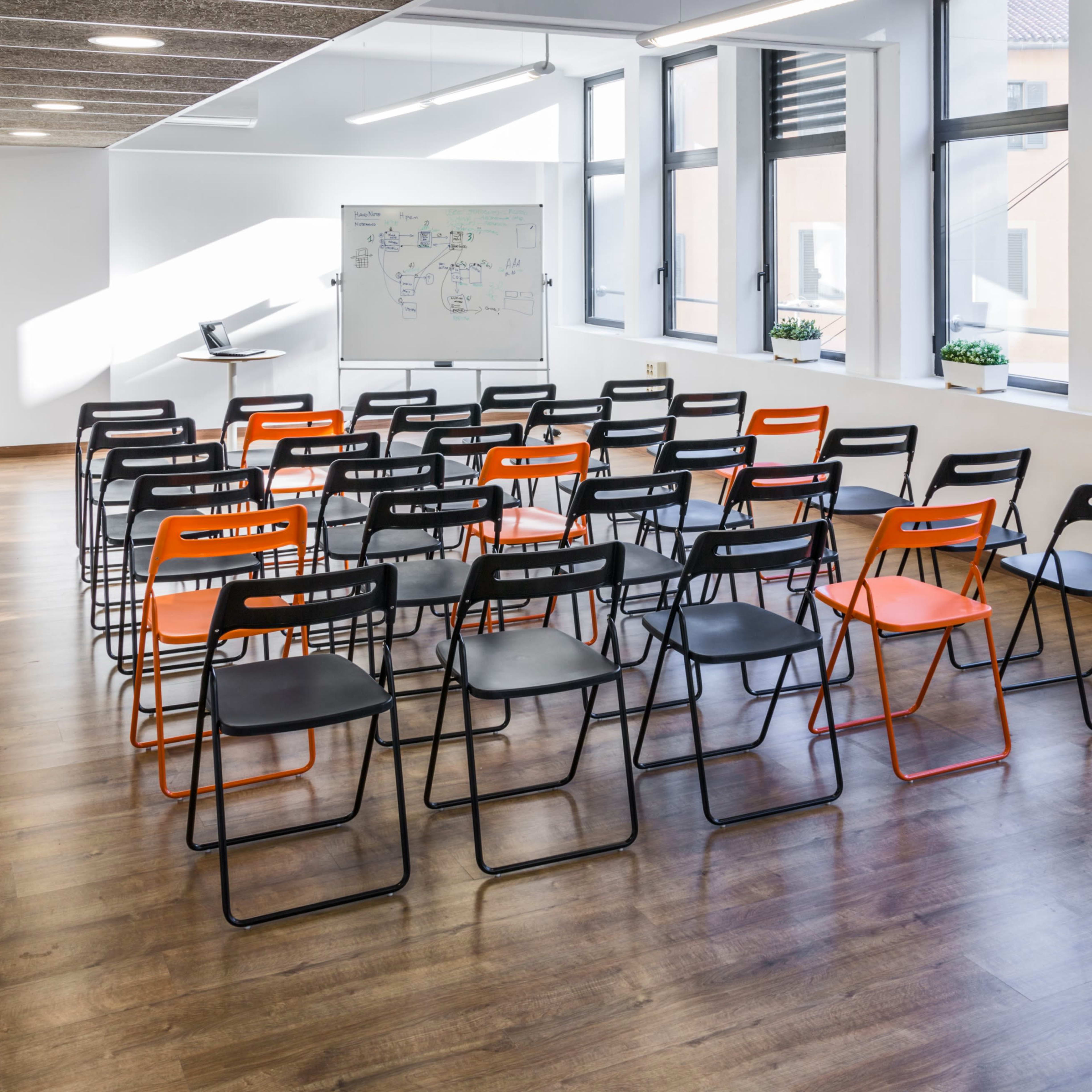 A row of black and orange chairs is arranged facing a whiteboard in a well-lit classroom.