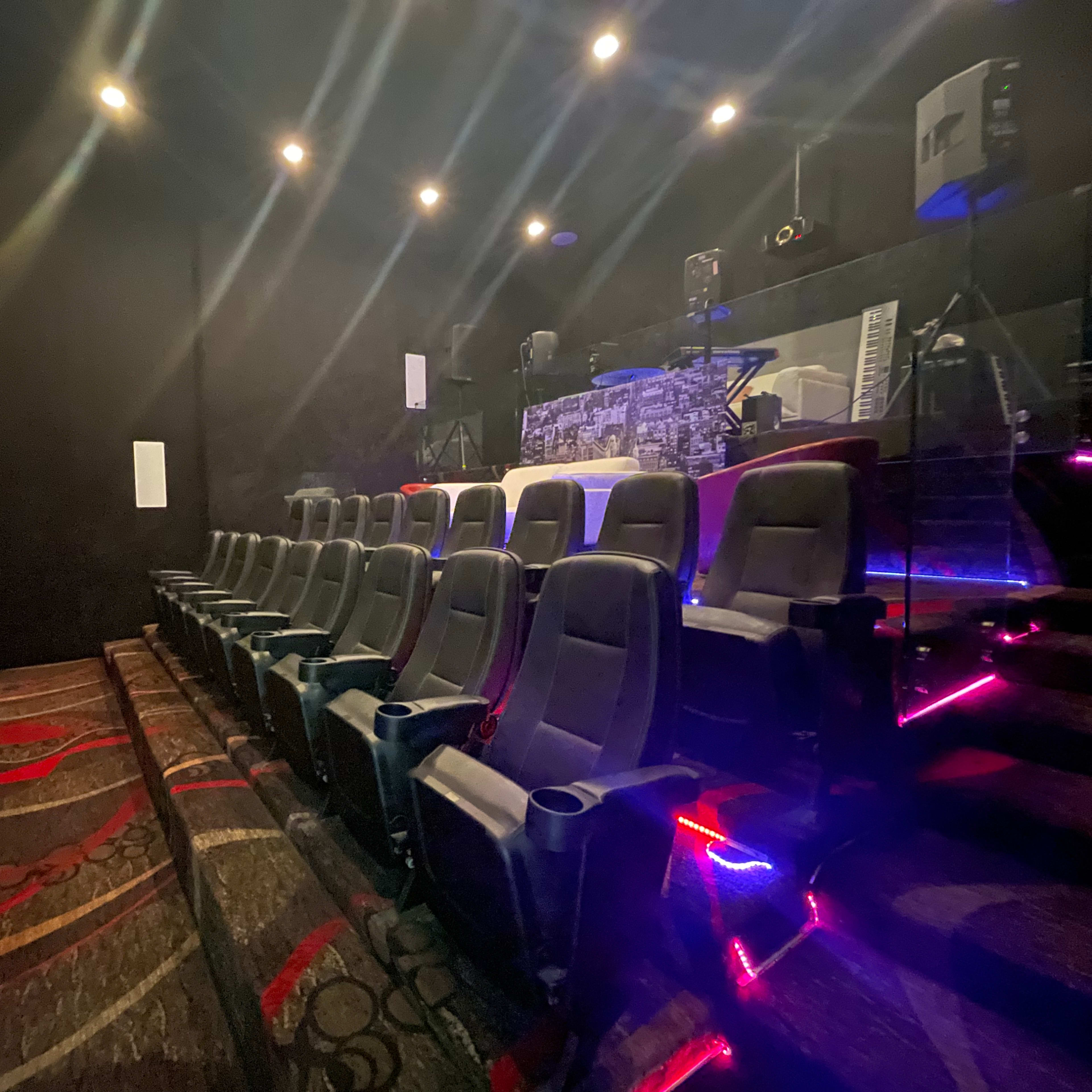 A row of empty theater seats in a dimly lit cinema with a stage in the background.