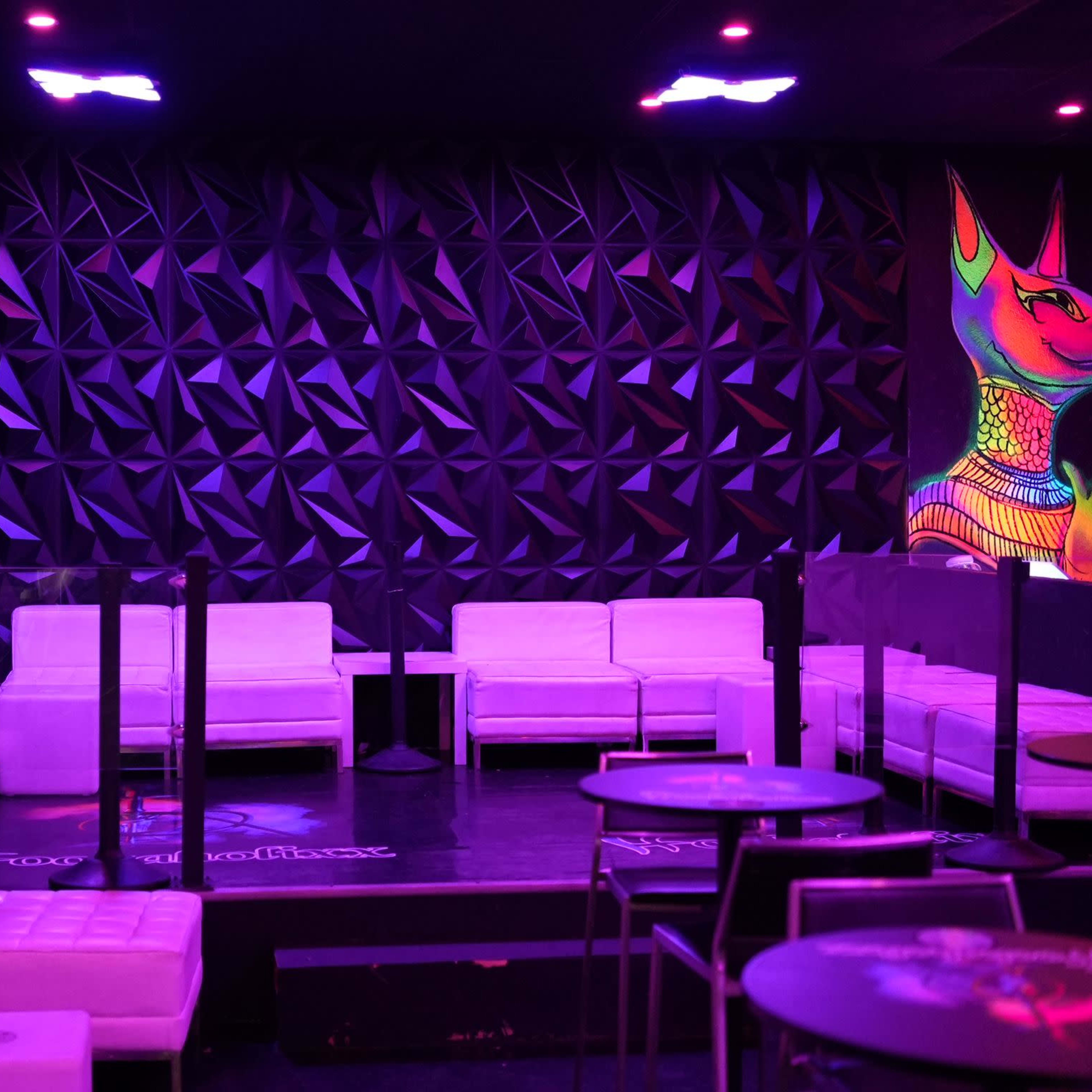 A lounge area with white seating and a colorful wall mural in a dimly lit setting.