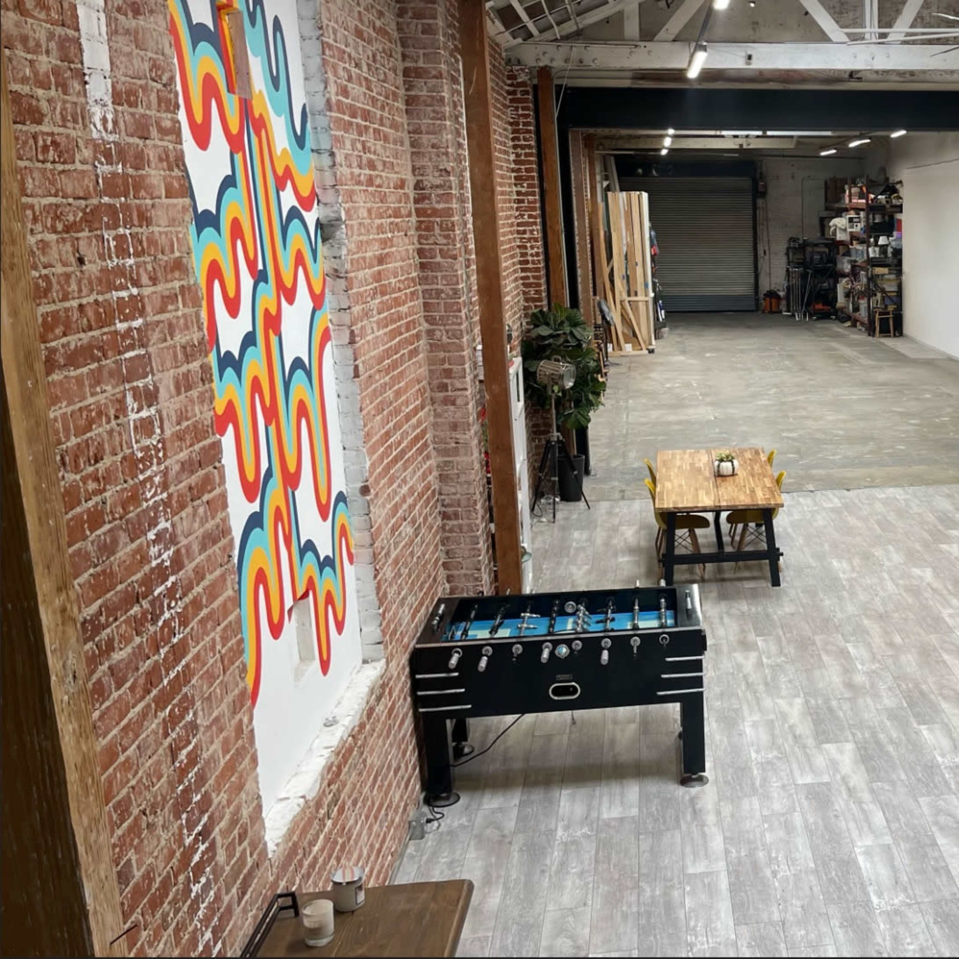 An open, spacious interior with exposed brick walls, a foosball table, a dining table, and a colorful retro refrigerator.