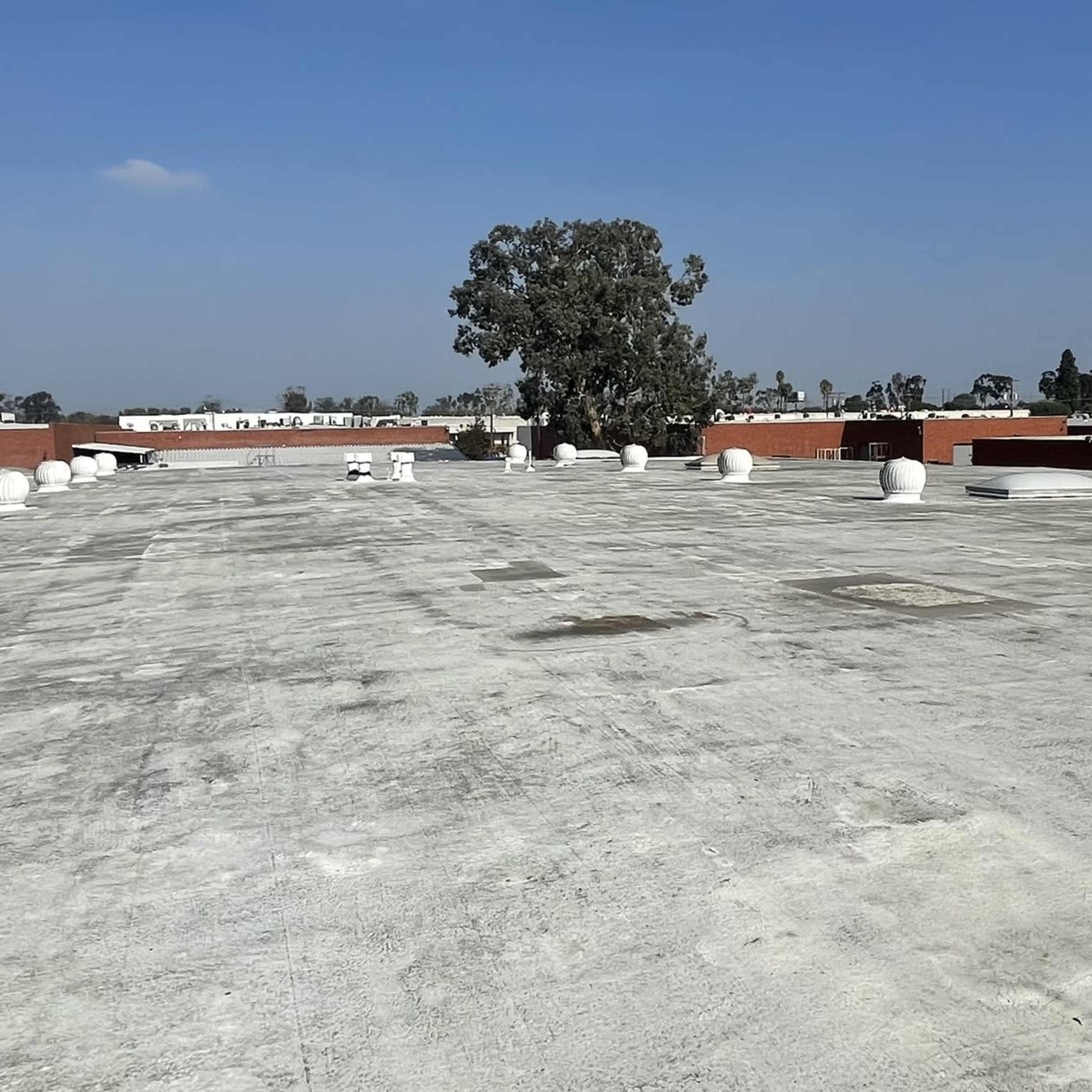 A flat rooftop featuring several ventilation units and a single tree in the background against a clear blue sky.