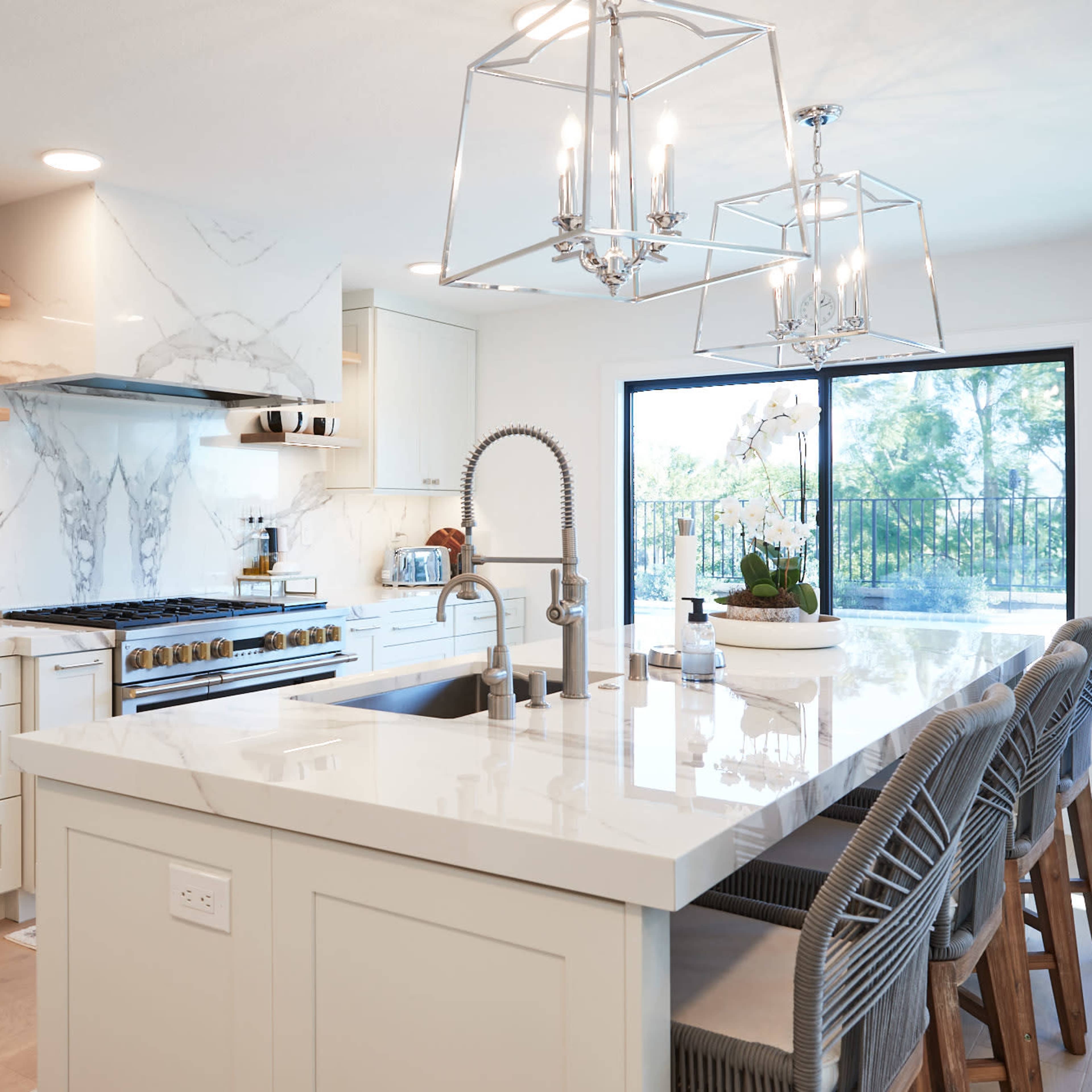 A modern kitchen featuring white cabinetry, a large marble island with bar stools, and a sliding glass door leading to an outdoor area.