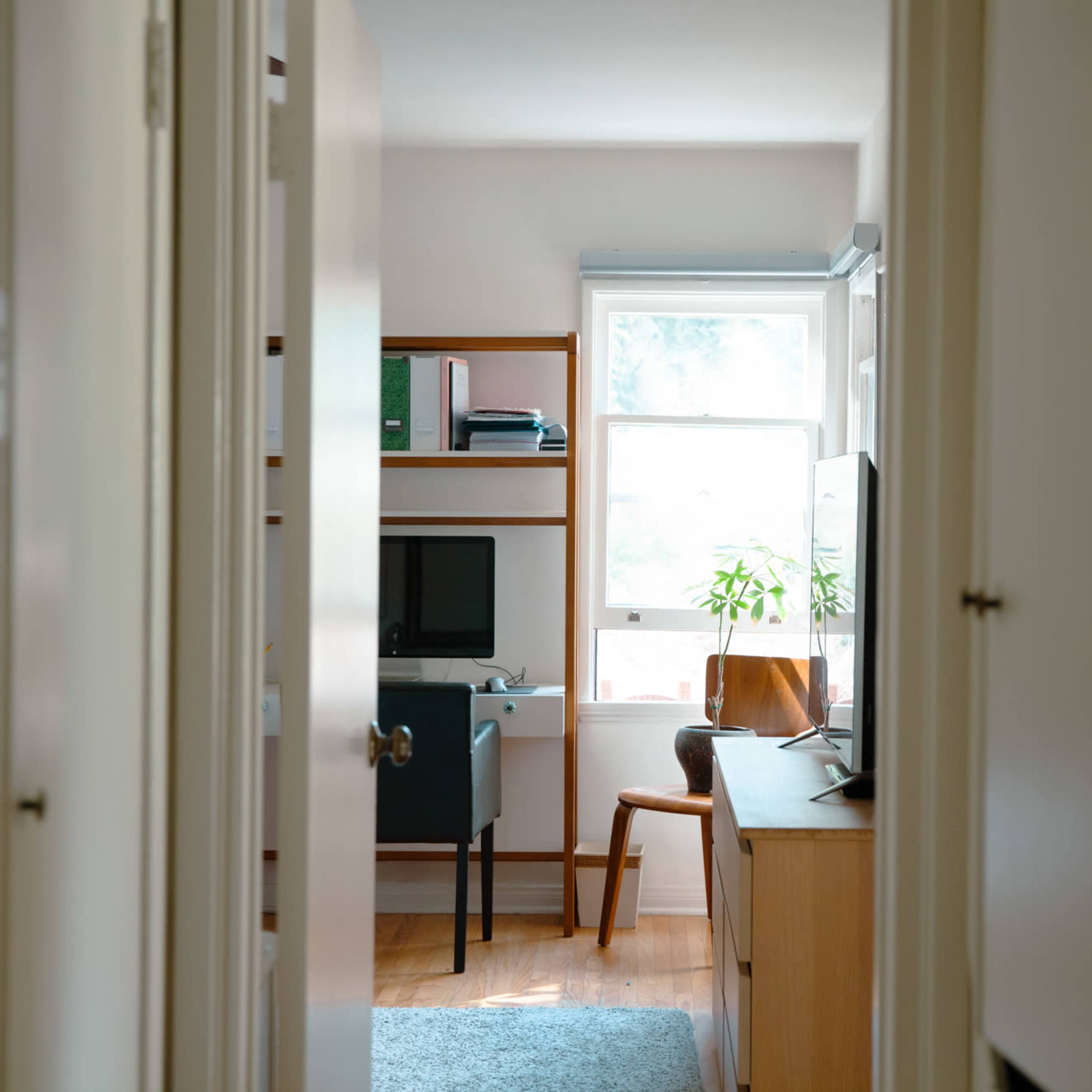 A narrow hallway leads to a small home office area with a desk, chair, and window.