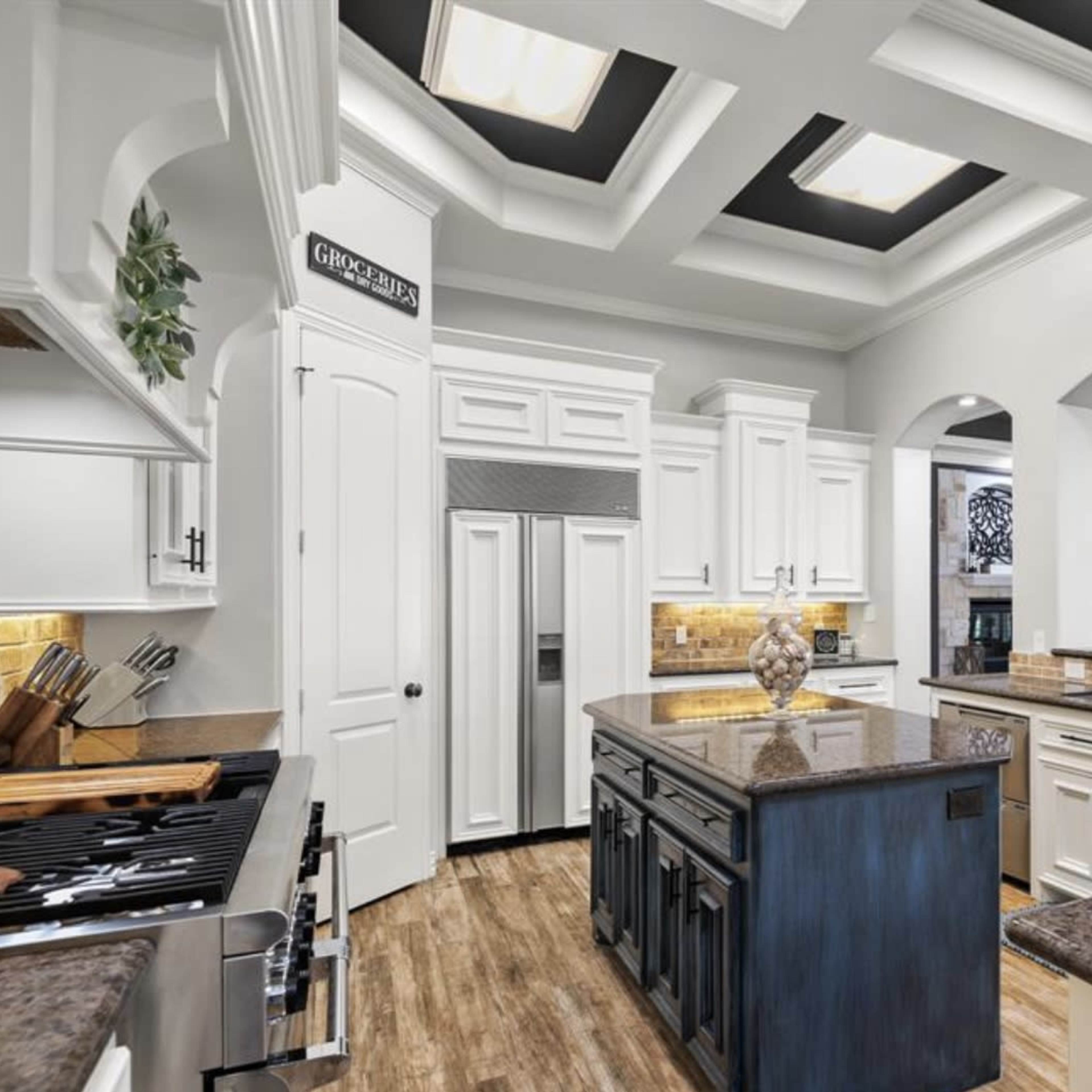 A modern kitchen with a coffered ceiling, granite countertops, white cabinetry, and stainless steel appliances.