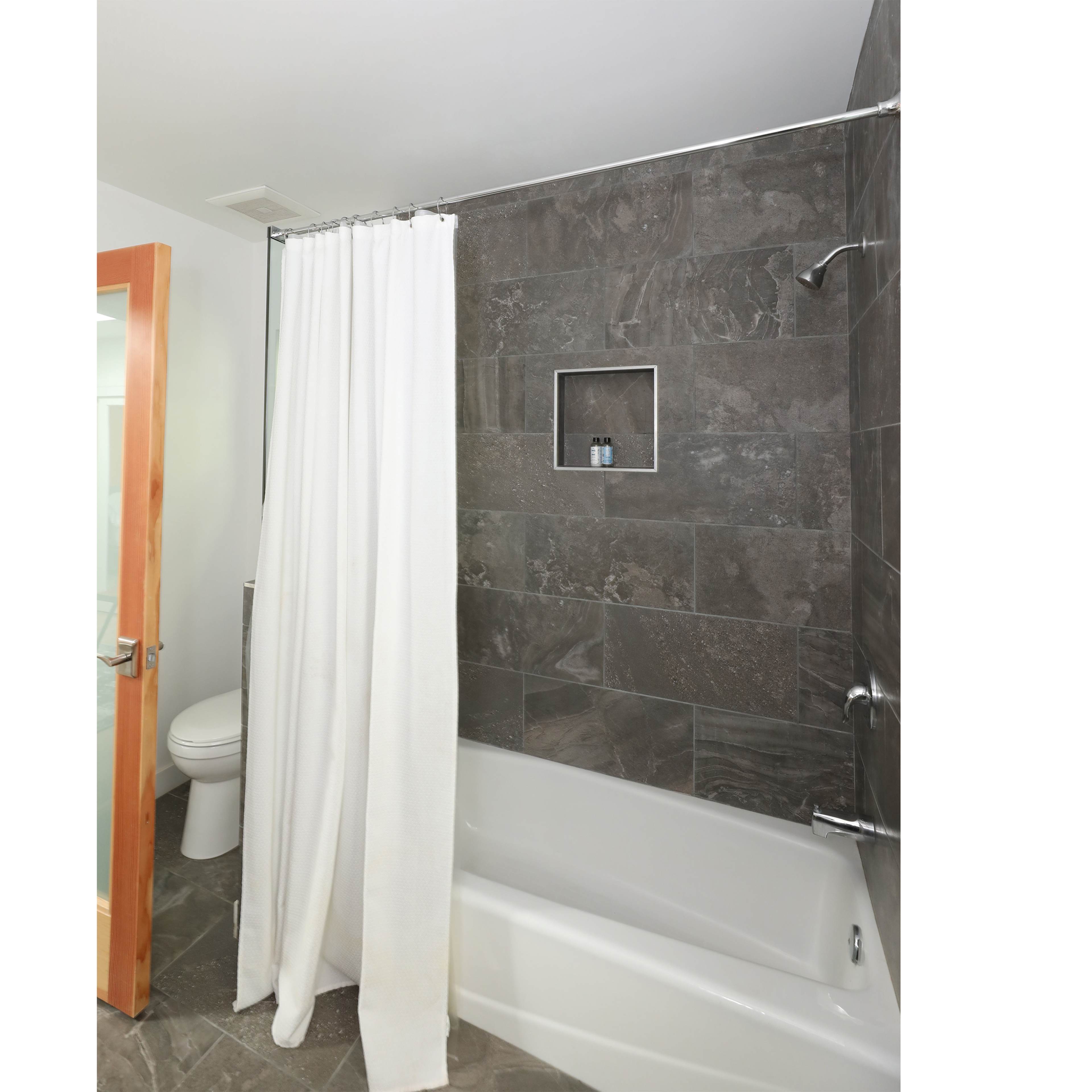 A bathroom features a bathtub with a shower curtain, tiled walls, and a toilet in the background.