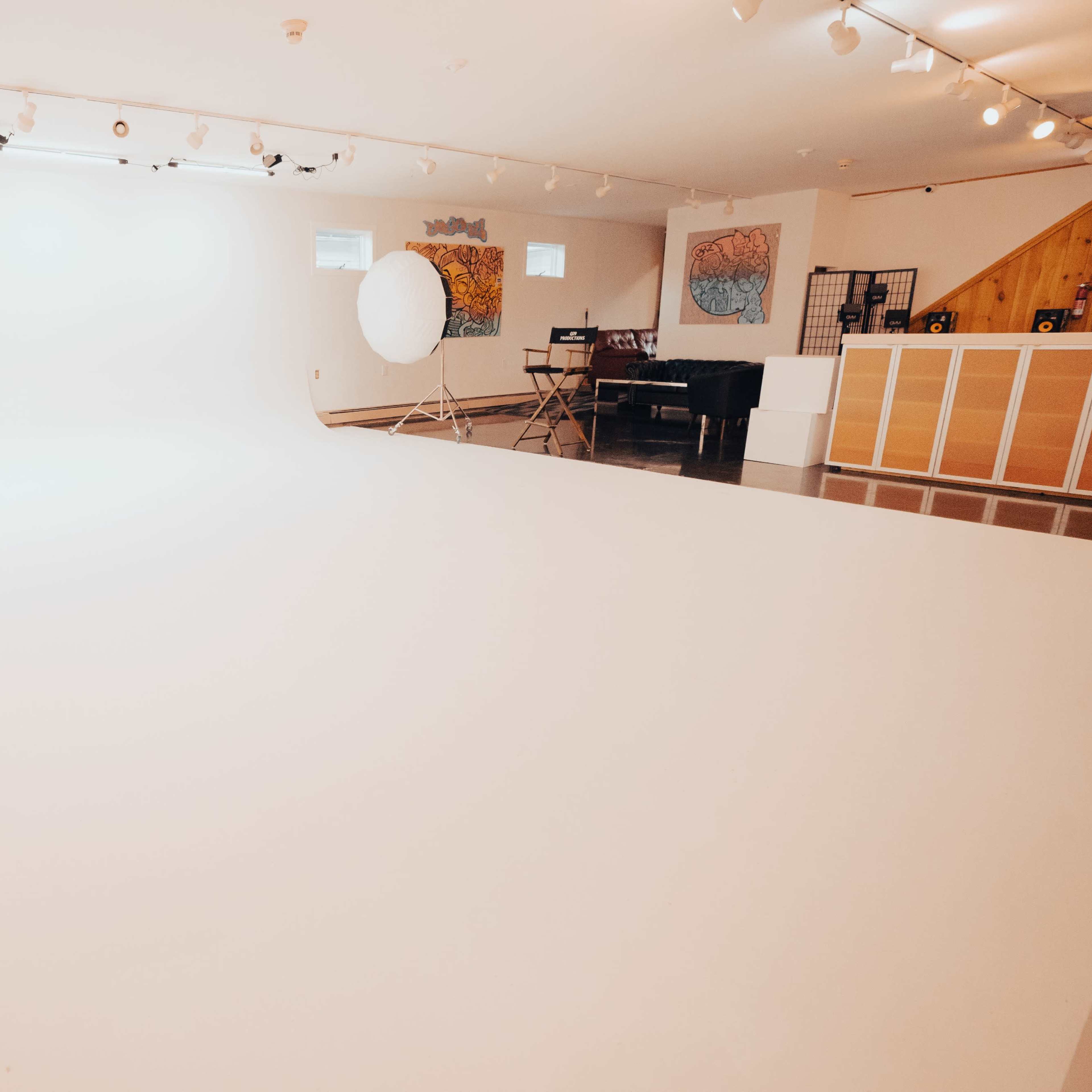 A spacious studio with a seamless white backdrop, soft lighting, and a few artistic decorations on the walls.