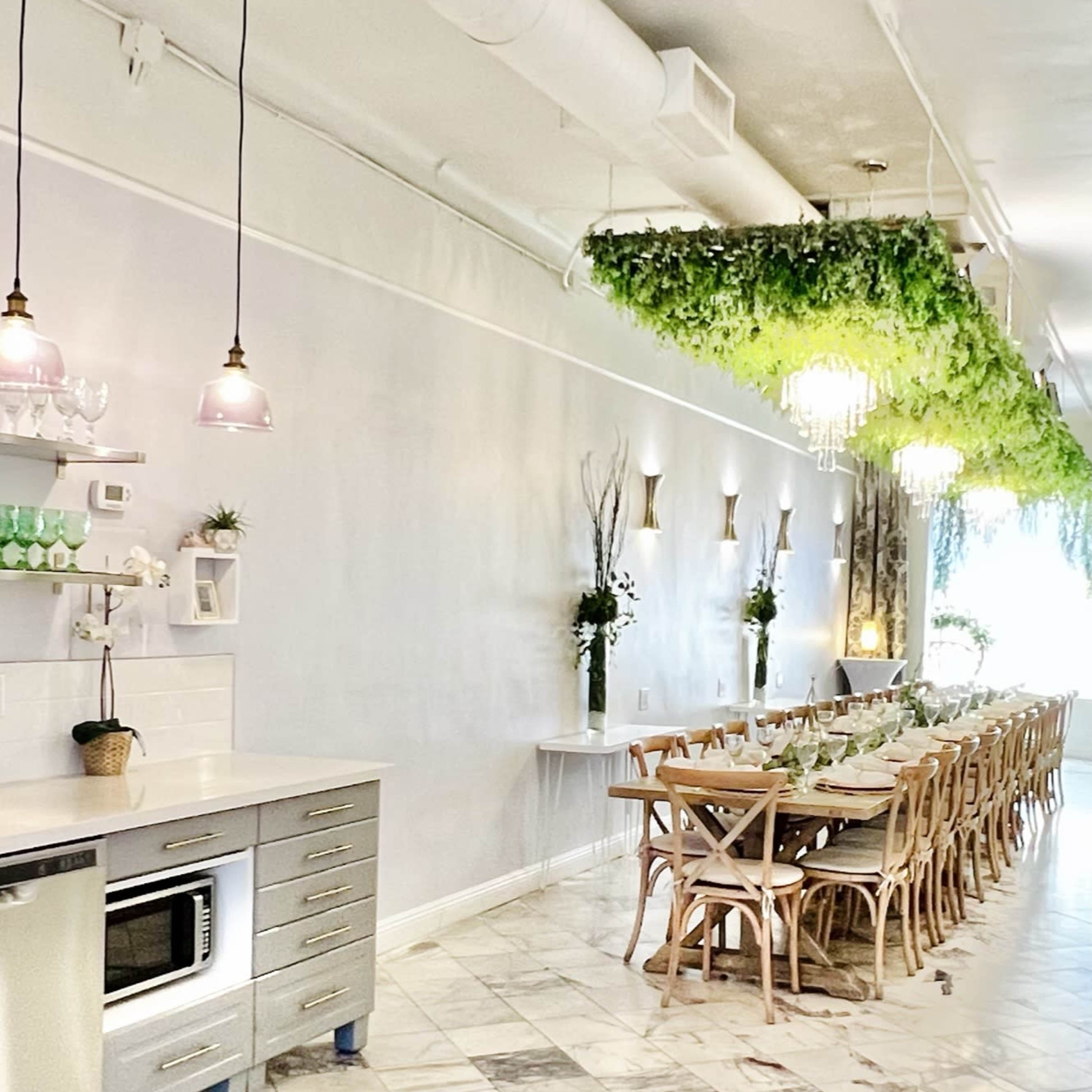 A spacious, elegantly designed dining area with a long wooden table, surrounded by chairs, and lush greenery hanging from the ceiling.