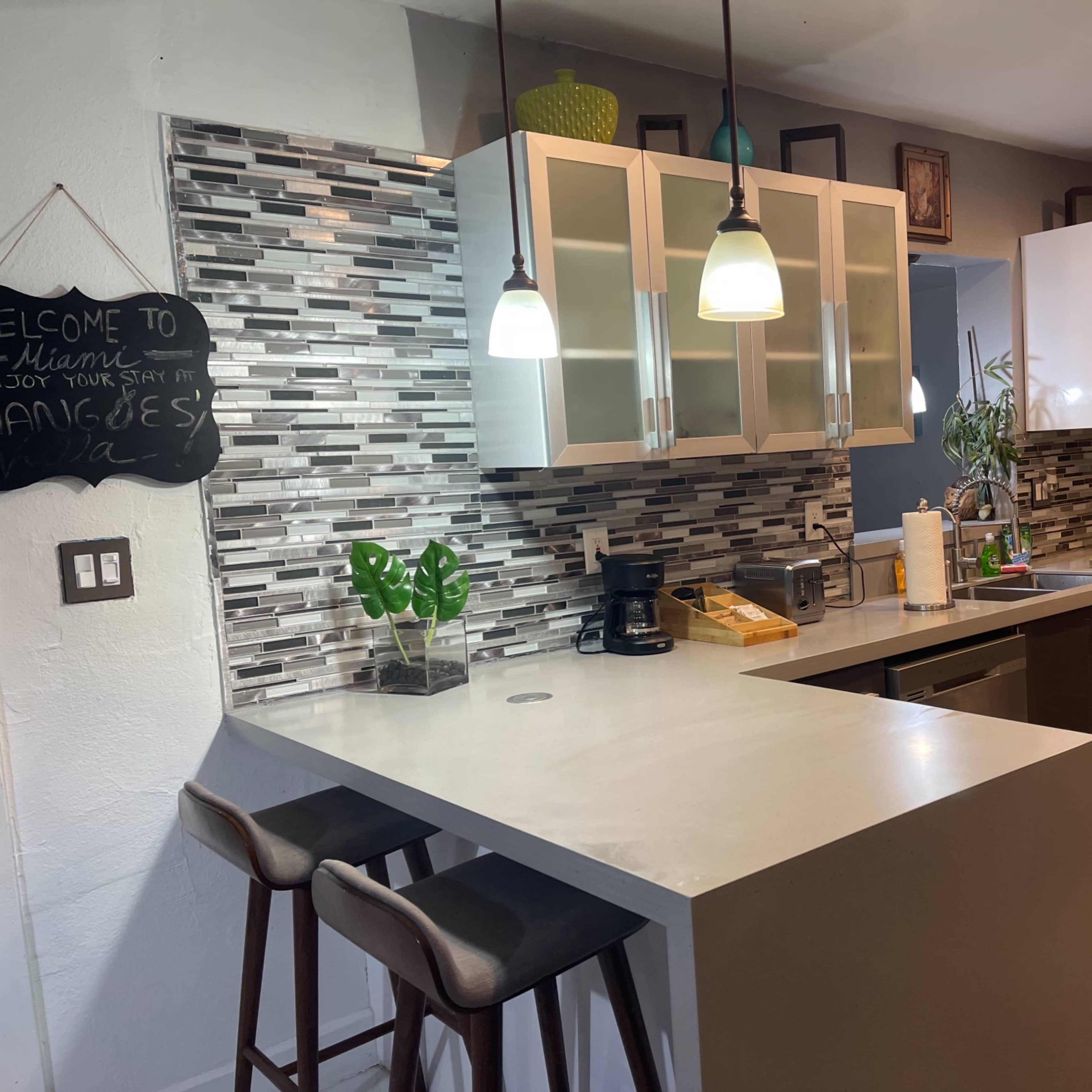 A modern kitchen featuring a central island with bar stools, sleek cabinetry, and a decorative tiled backsplash.