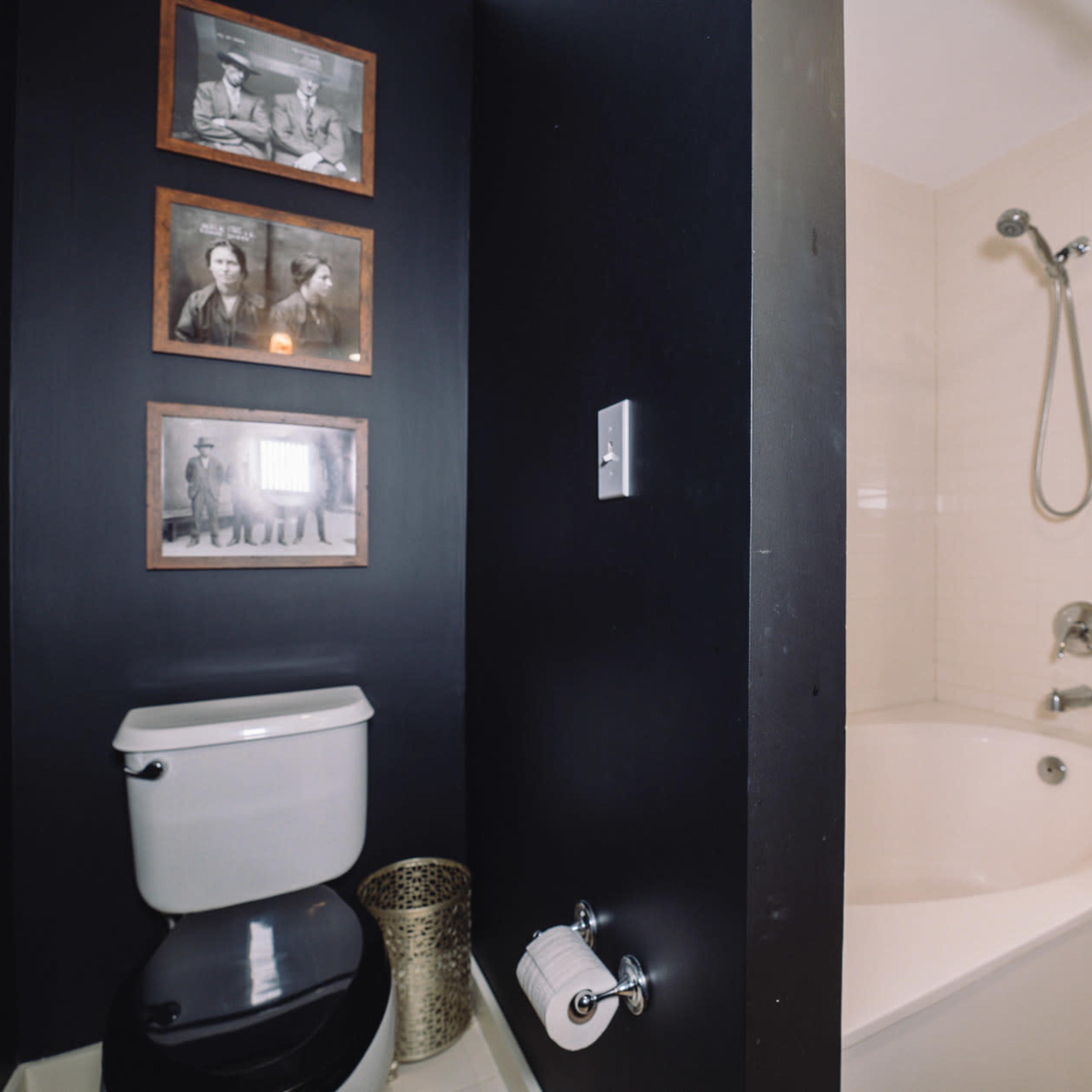 A bathroom features a toilet beside a shower and a bathtub, with framed black-and-white photographs hanging on the wall.