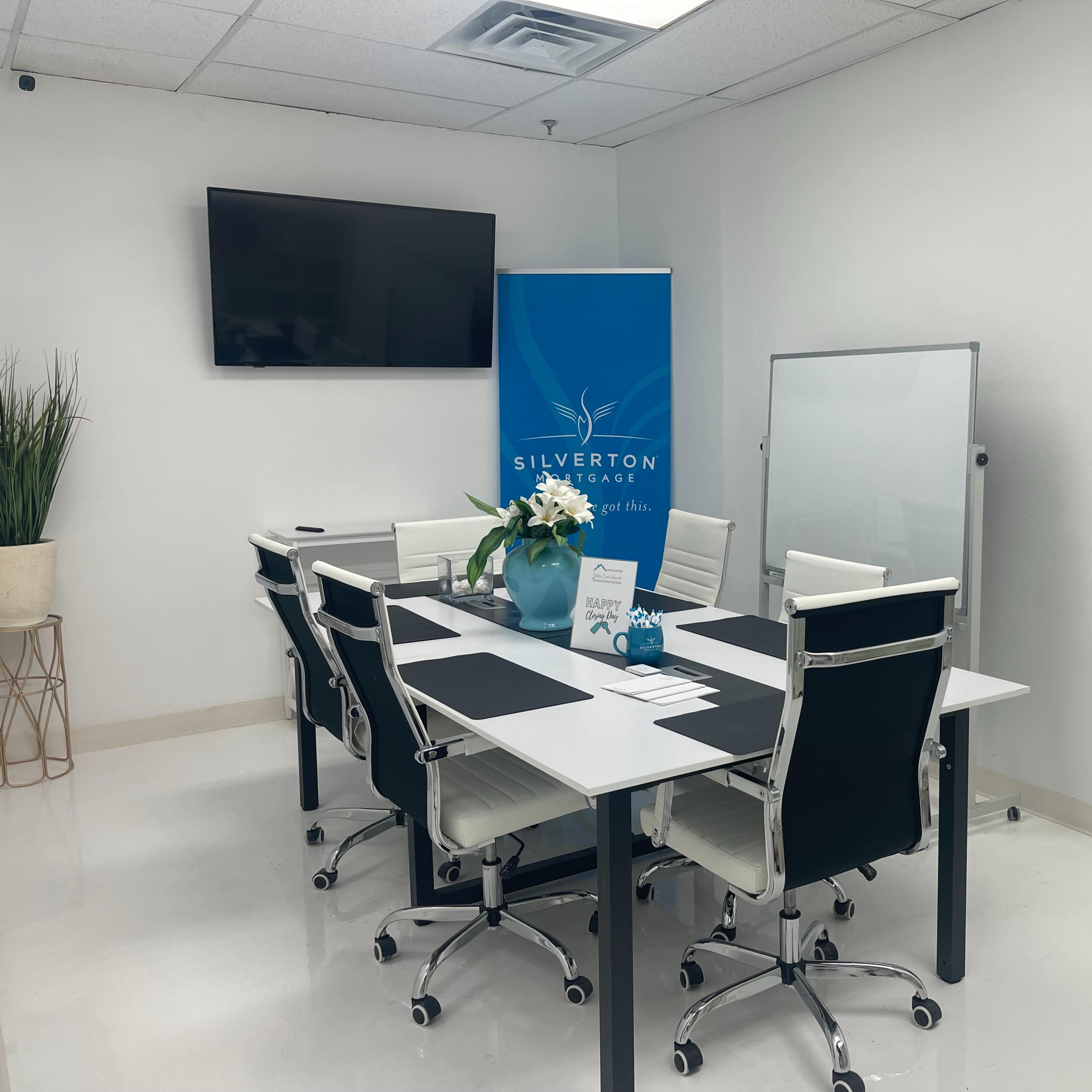 A modern conference room is set up with a large table, white chairs, a flat-screen TV, a whiteboard, and a display banner for Silverton Financial.