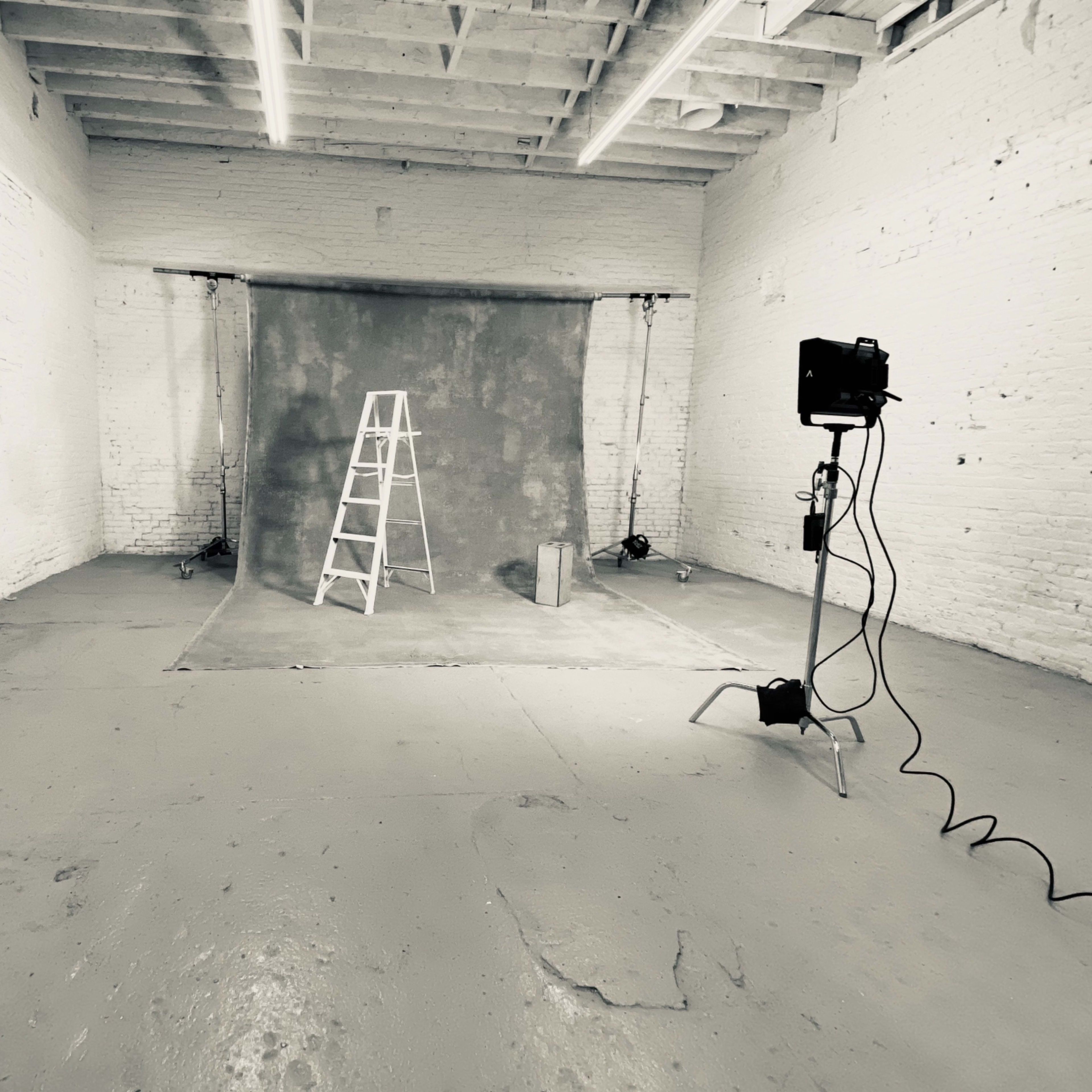 An empty photography studio with a ladder, backdrop, and light setup.