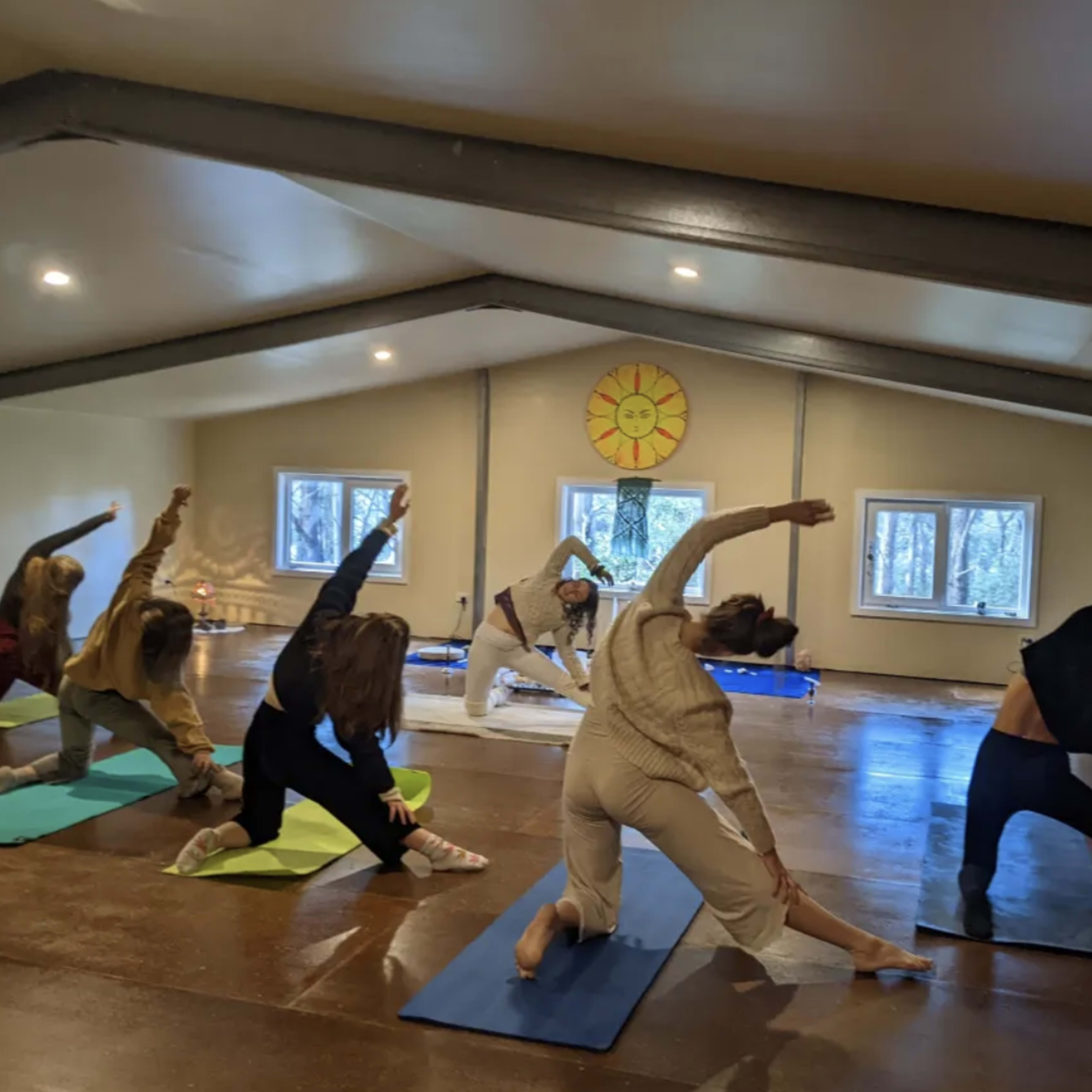 A group of six individuals are practicing yoga on mats in a spacious, well-lit studio.