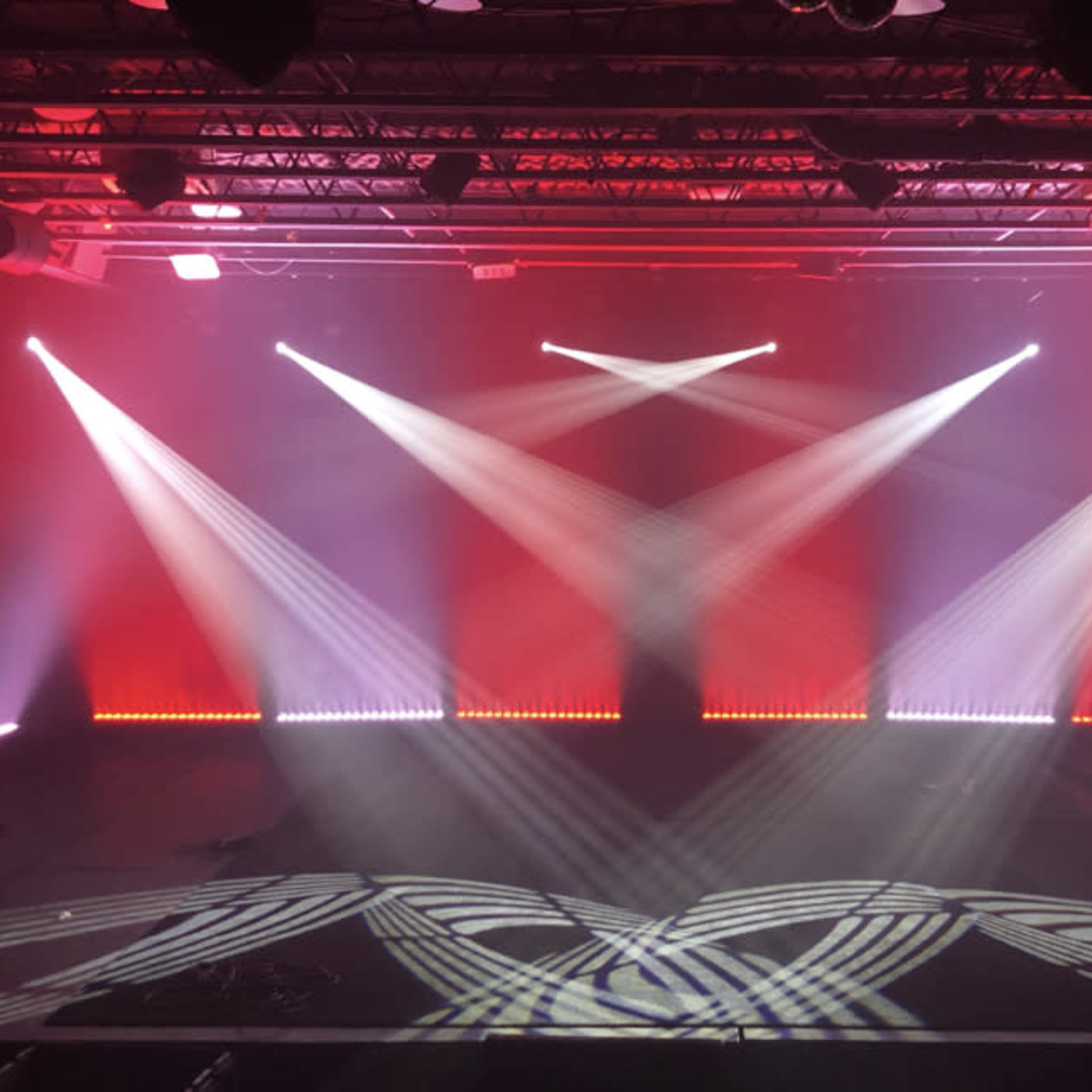 A stage setup with dynamic lighting effects and a black floor, featuring beams of light projected in various directions against a backdrop.