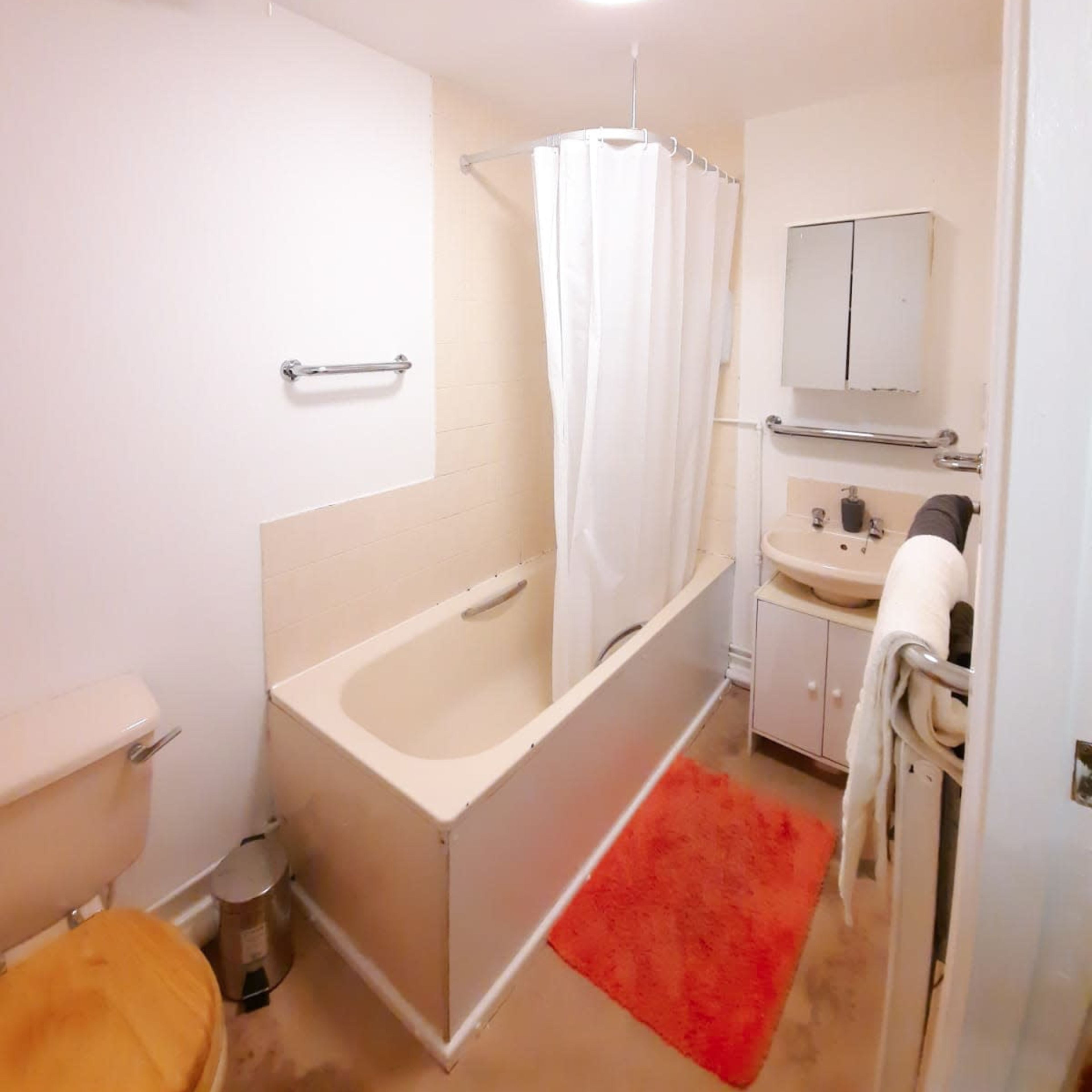 A bathroom with a bathtub, a shower curtain, a toilet, a sink with a cabinet, and a bright ceiling light.
