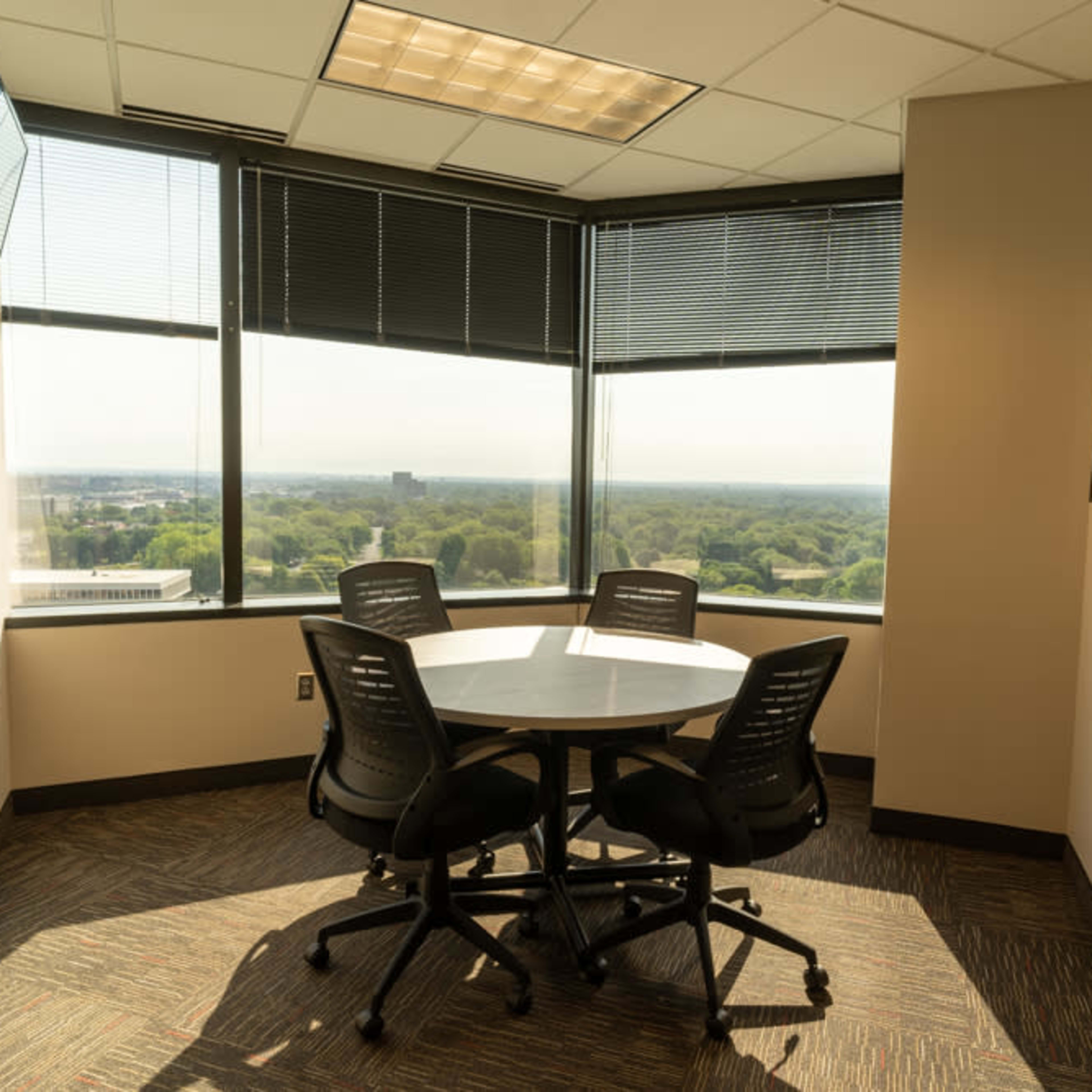 A small conference room with a round table and four chairs is situated in a corner, featuring large windows that offer a view of the surrounding landscape.