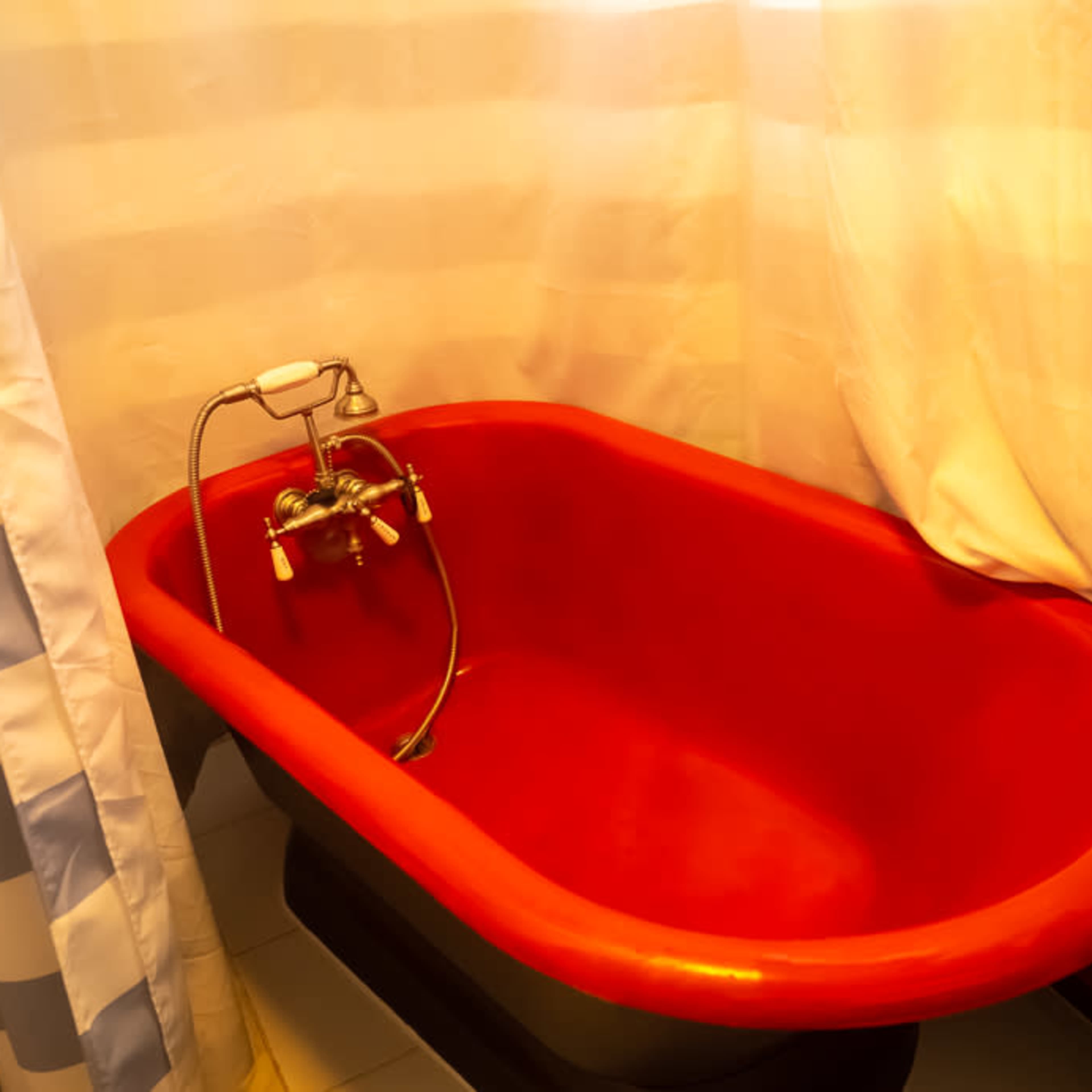 A red tub with a faucet and showerhead, situated in a bathroom enclosed by striped curtains.