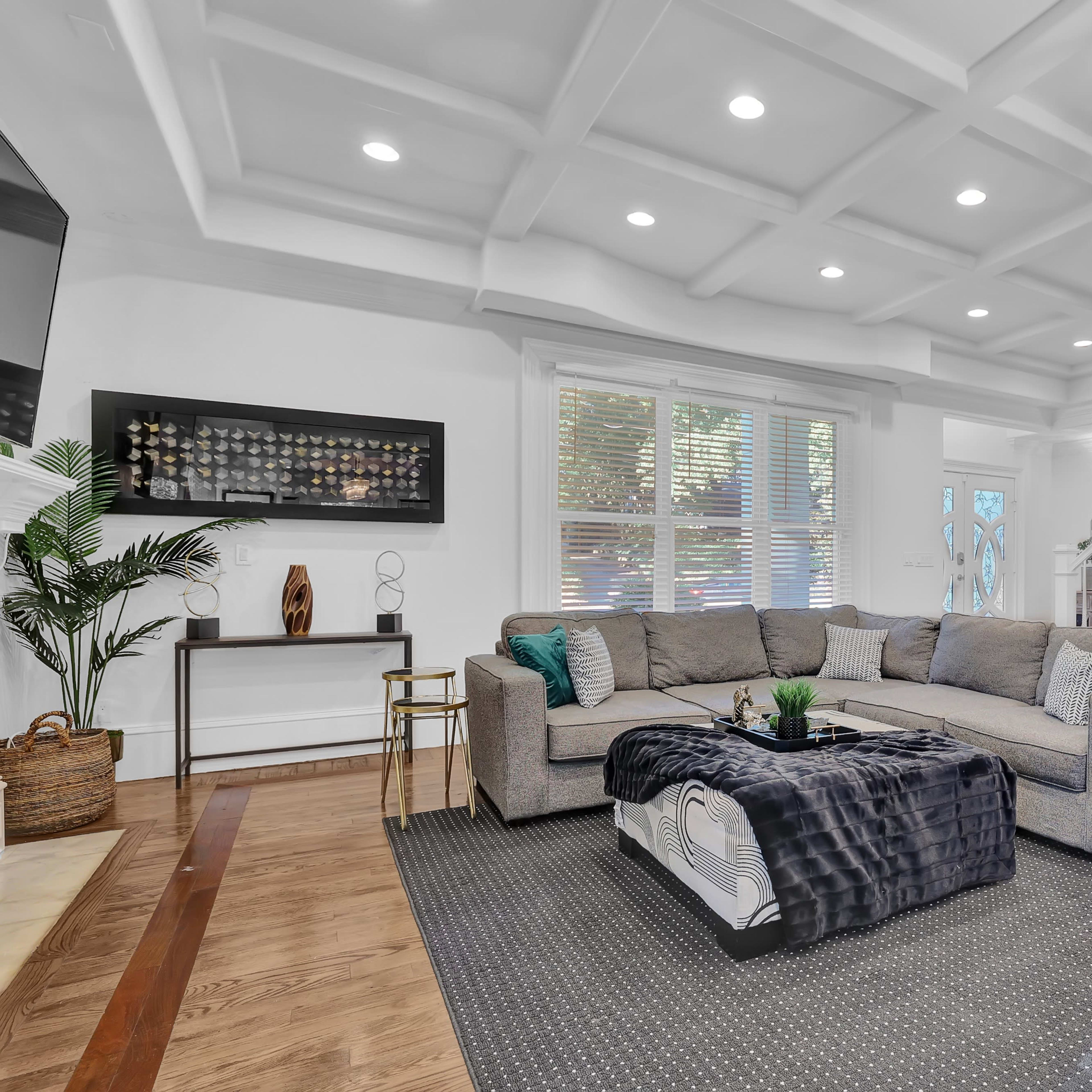 A modern living room with a spacious gray sectional sofa, a coffee table, and stylish decor under a coffered ceiling with recessed lighting.