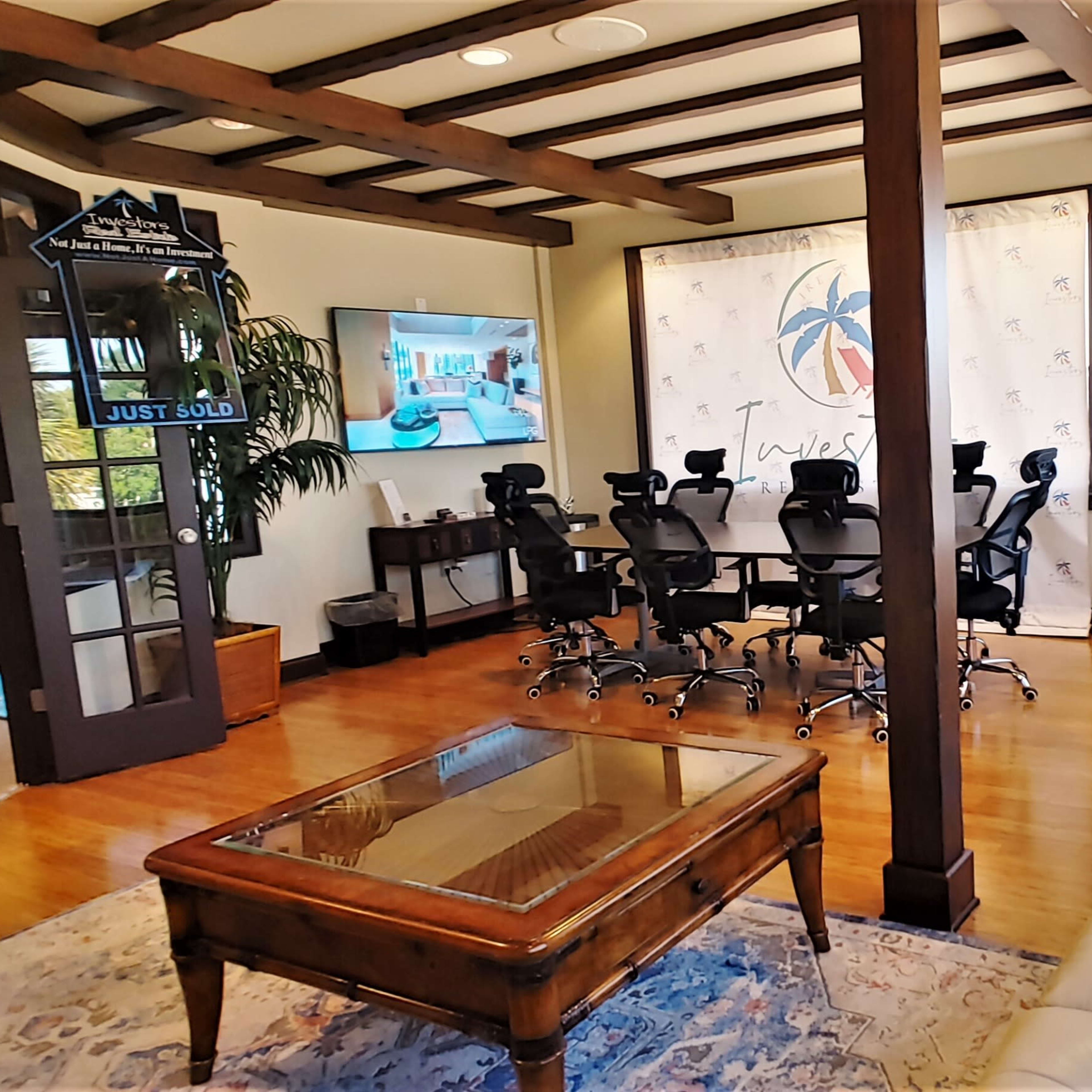 A modern office space featuring a conference room with a large table and ergonomic chairs, a reception area with a television, and large windows letting in natural light.