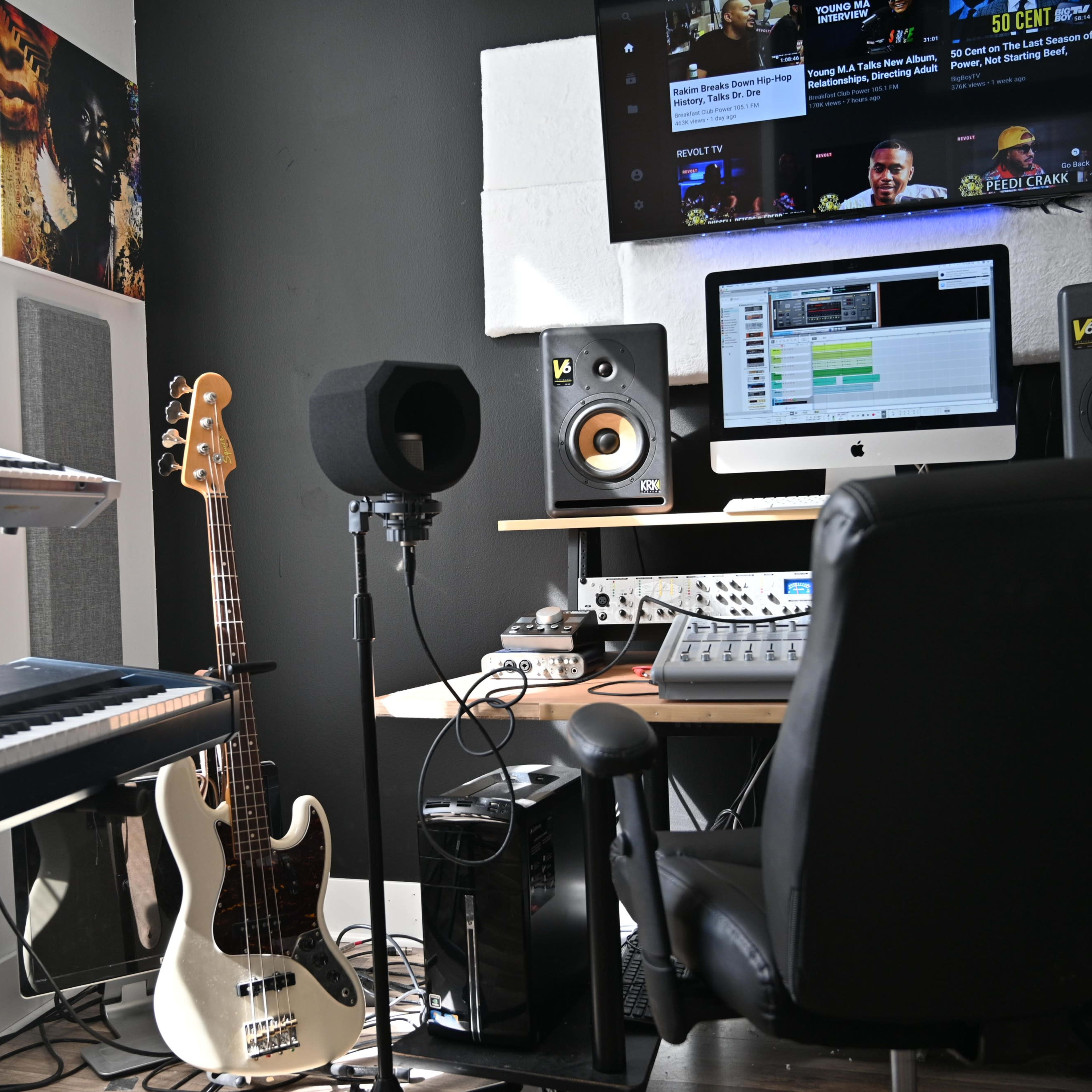 A music production studio features a keyboard, a bass guitar, a computer with recording software, and a microphone setup.
