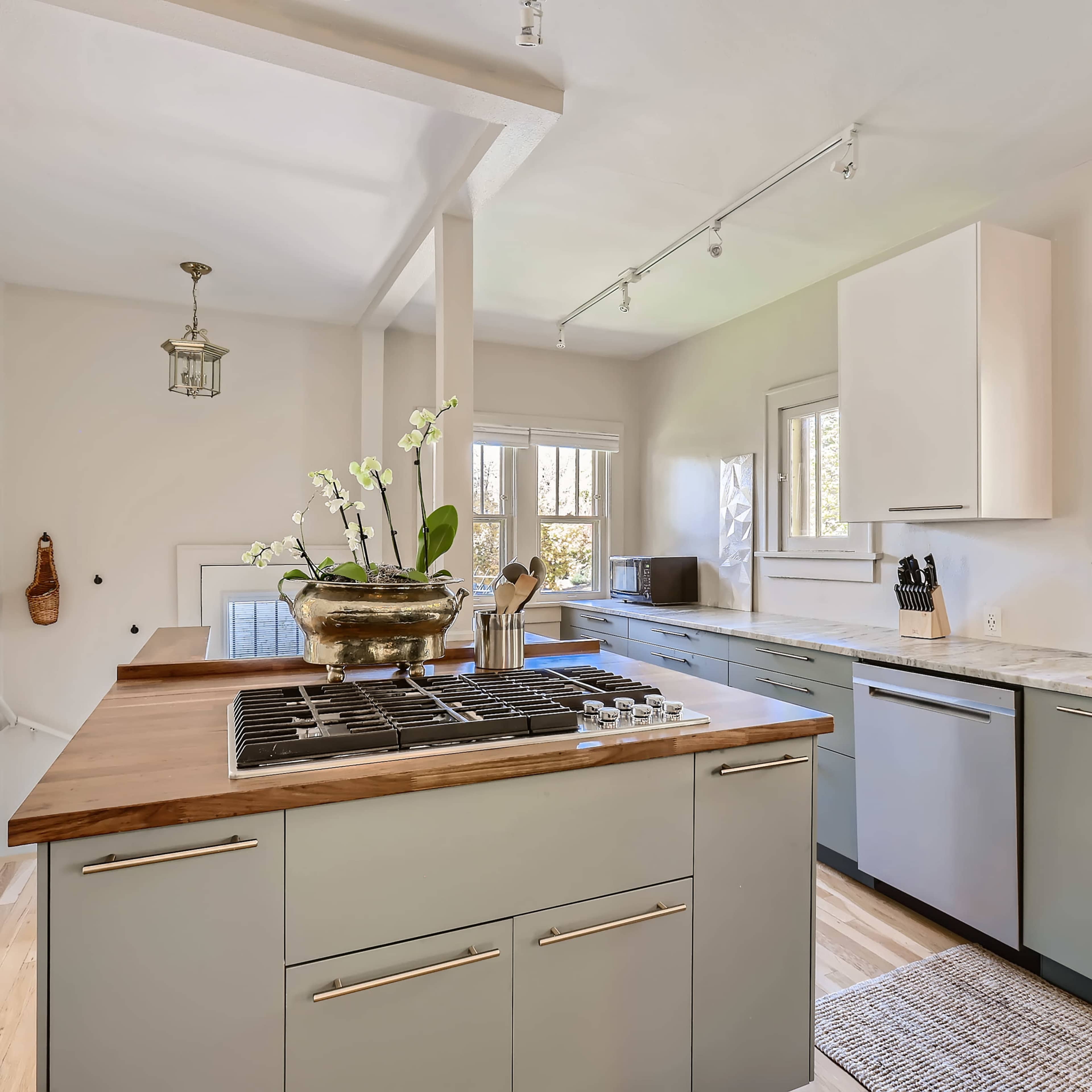 The modern kitchen features a central island with a gas cooktop, light green cabinetry, and large windows that welcome natural light.