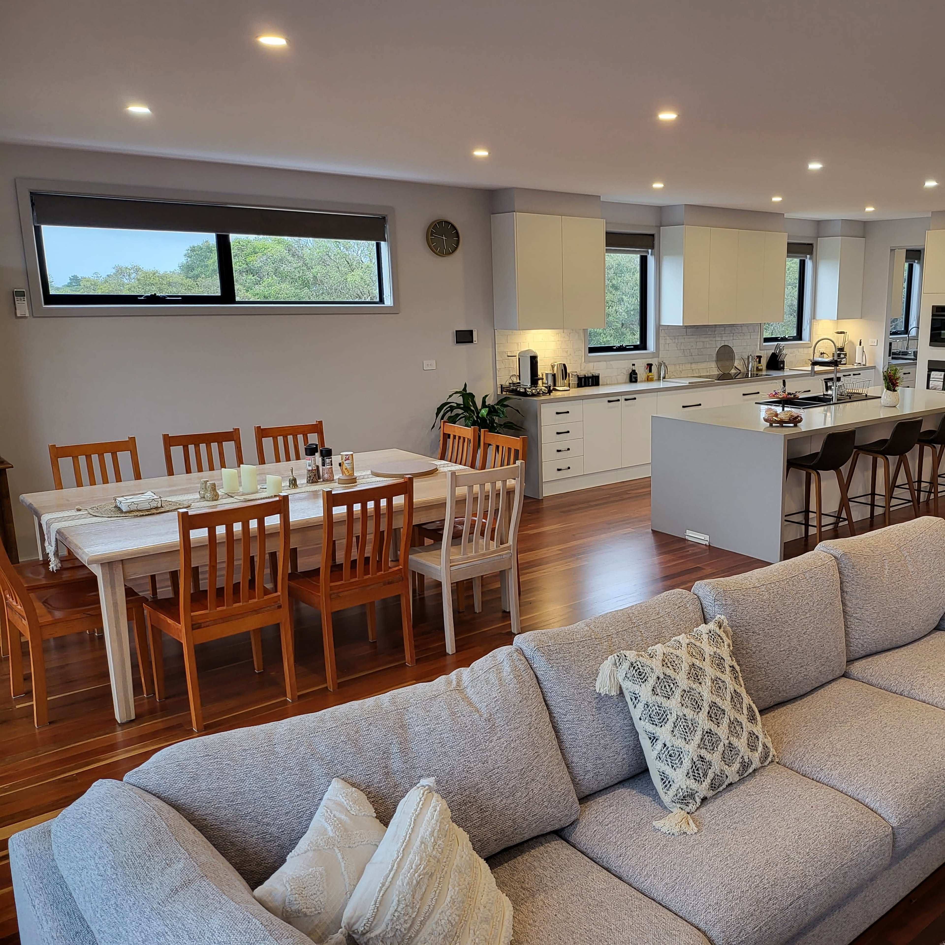 A modern open-plan living space features a kitchen, dining area with a table, and a comfortable sofa arrangement.