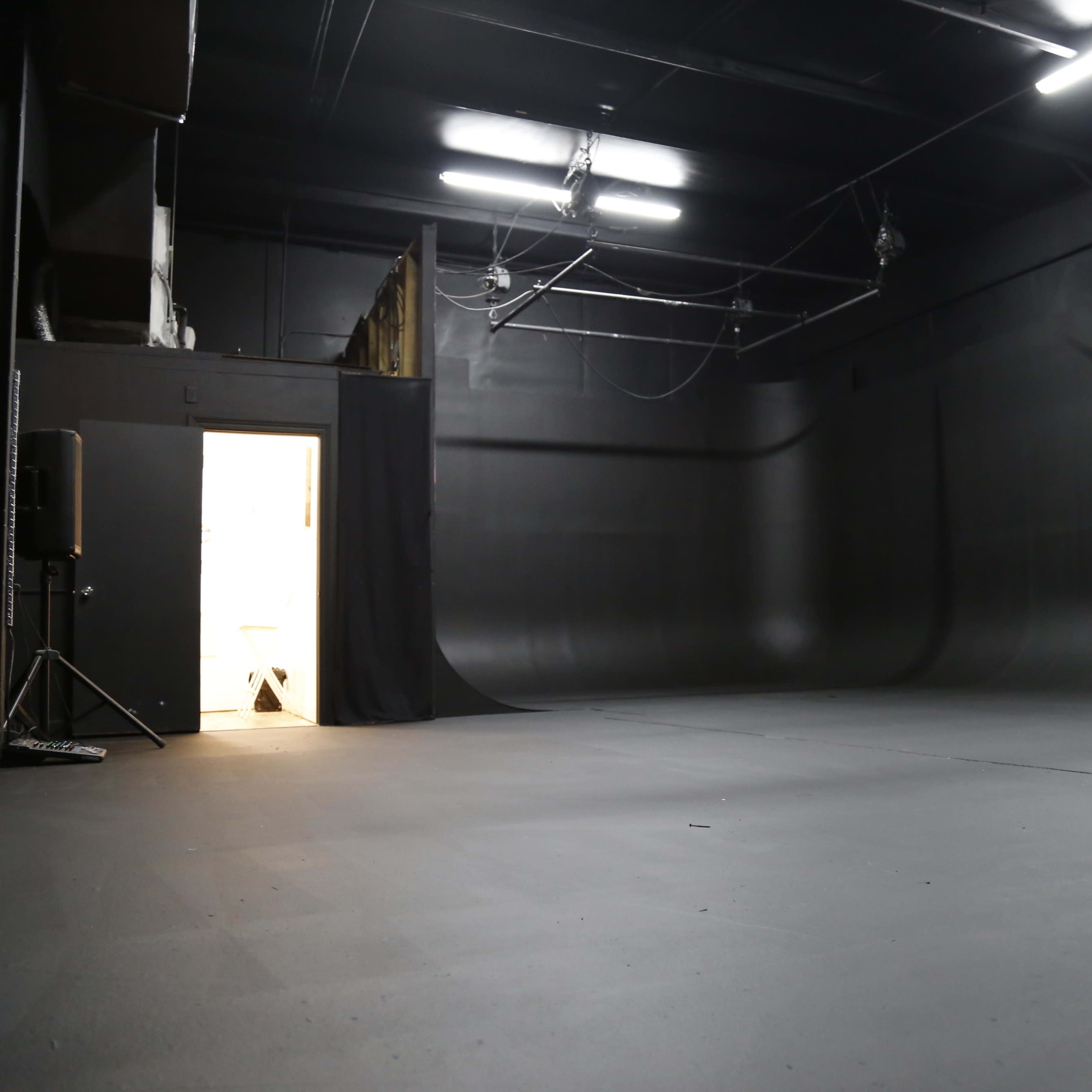 A large, empty black studio space with a door partially open at one end.