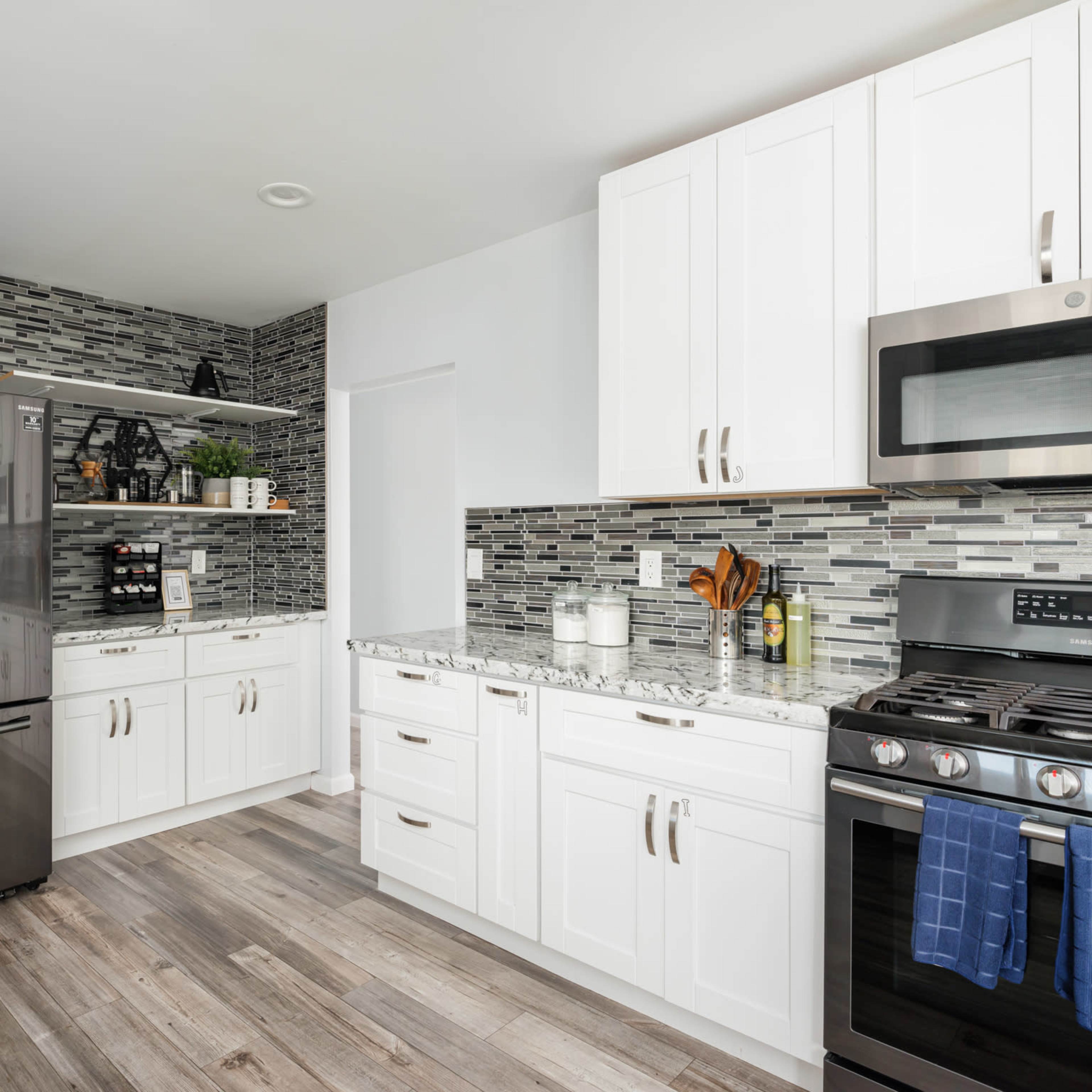 A modern kitchen with white cabinets, a granite countertop, and stainless steel appliances, including a refrigerator and a gas stove.