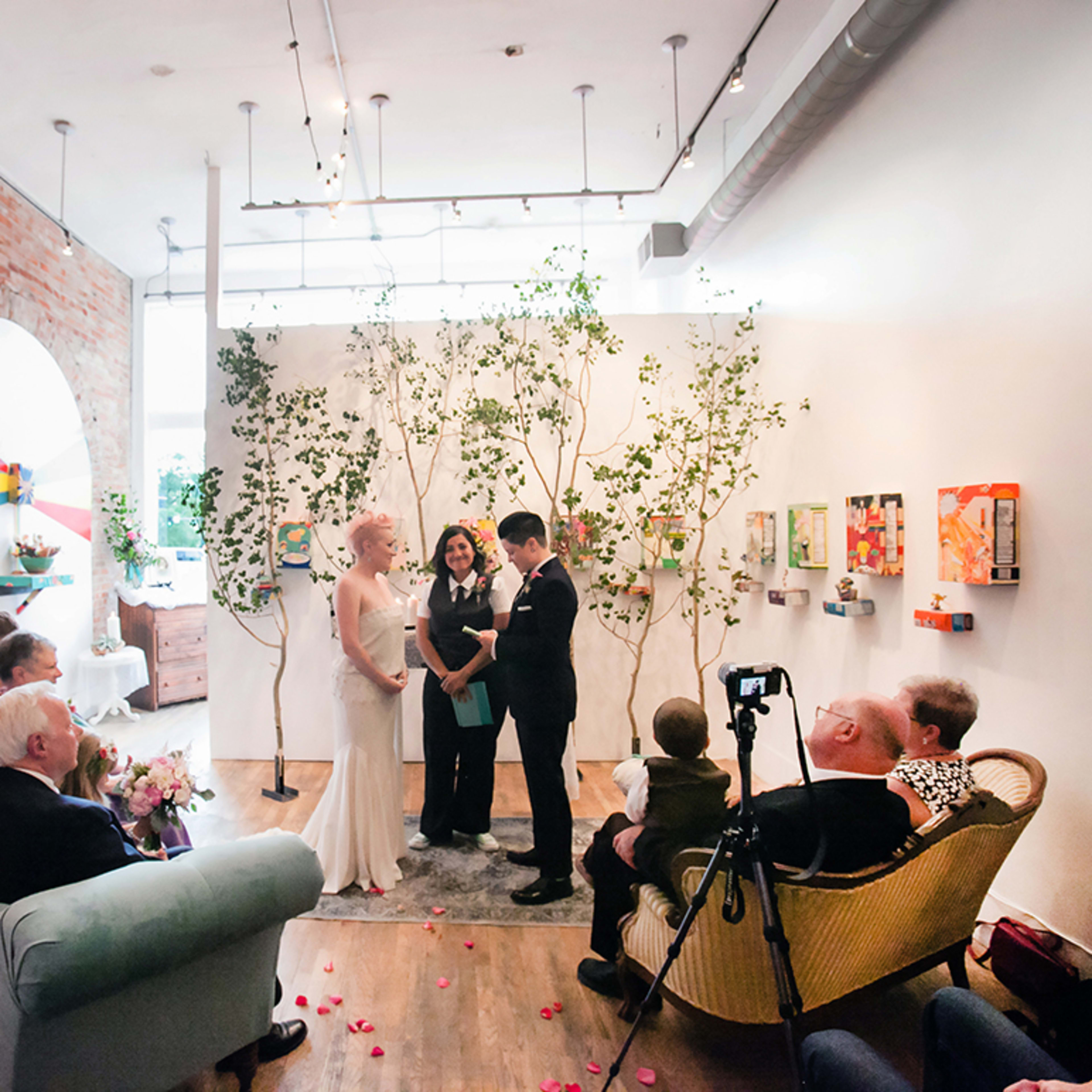 A couple stands in front of a small gathering of guests during a wedding ceremony in a decorated indoor setting.