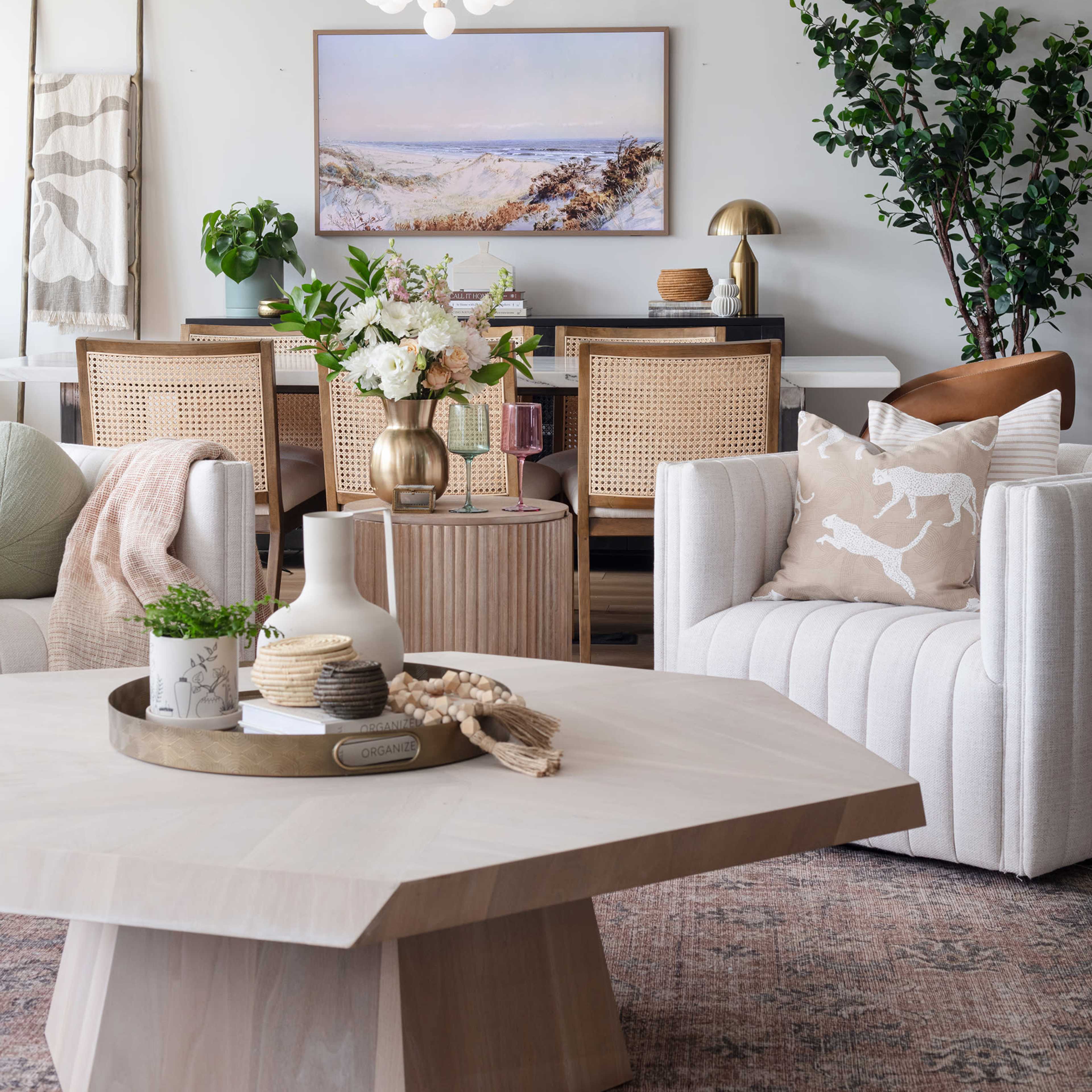 A modern living space features a light-filled room with a wooden coffee table, a dining area in the background, and decorative plants.