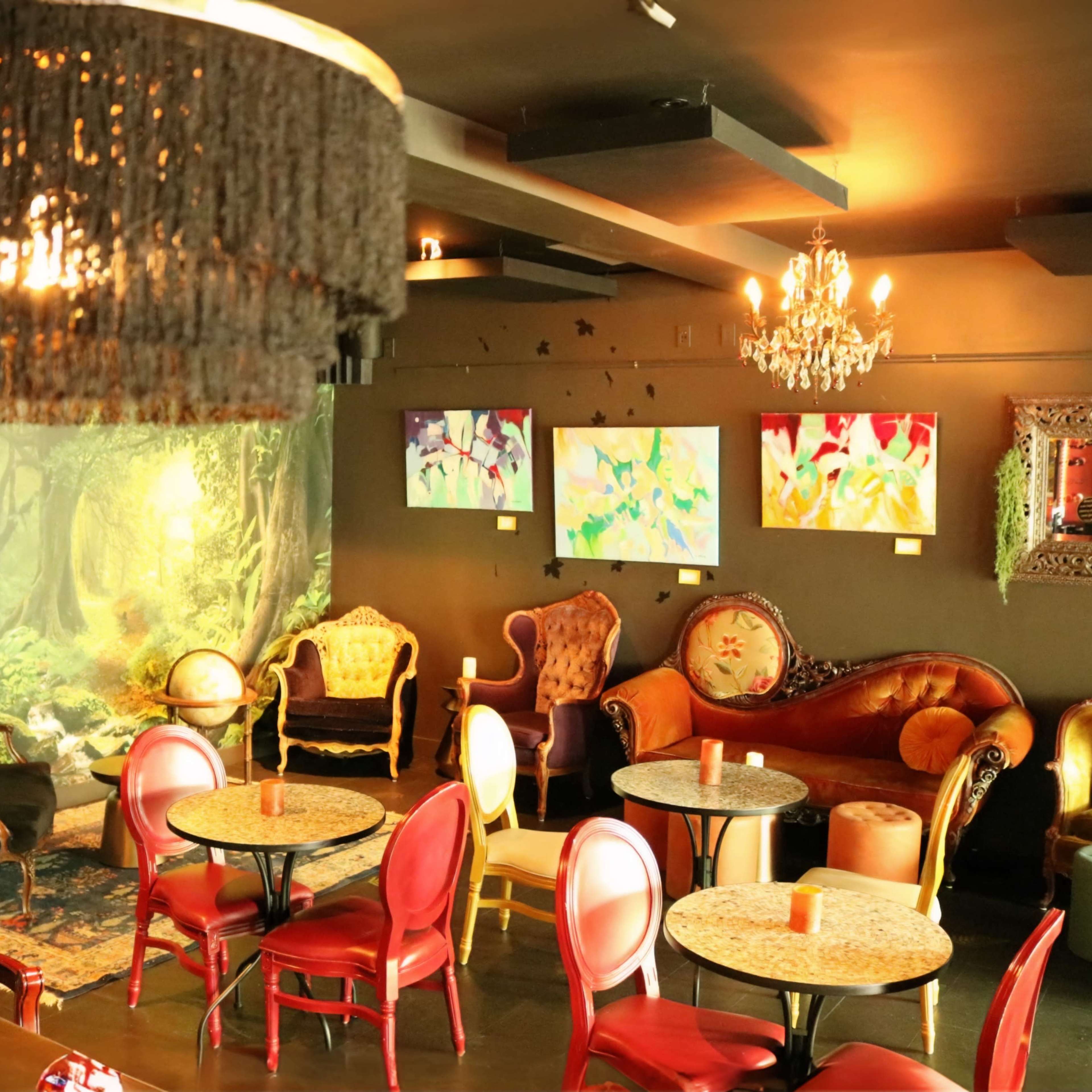 A cozy café interior with ornate seating, colorful artworks on the walls, and a scenic backdrop of a forest.