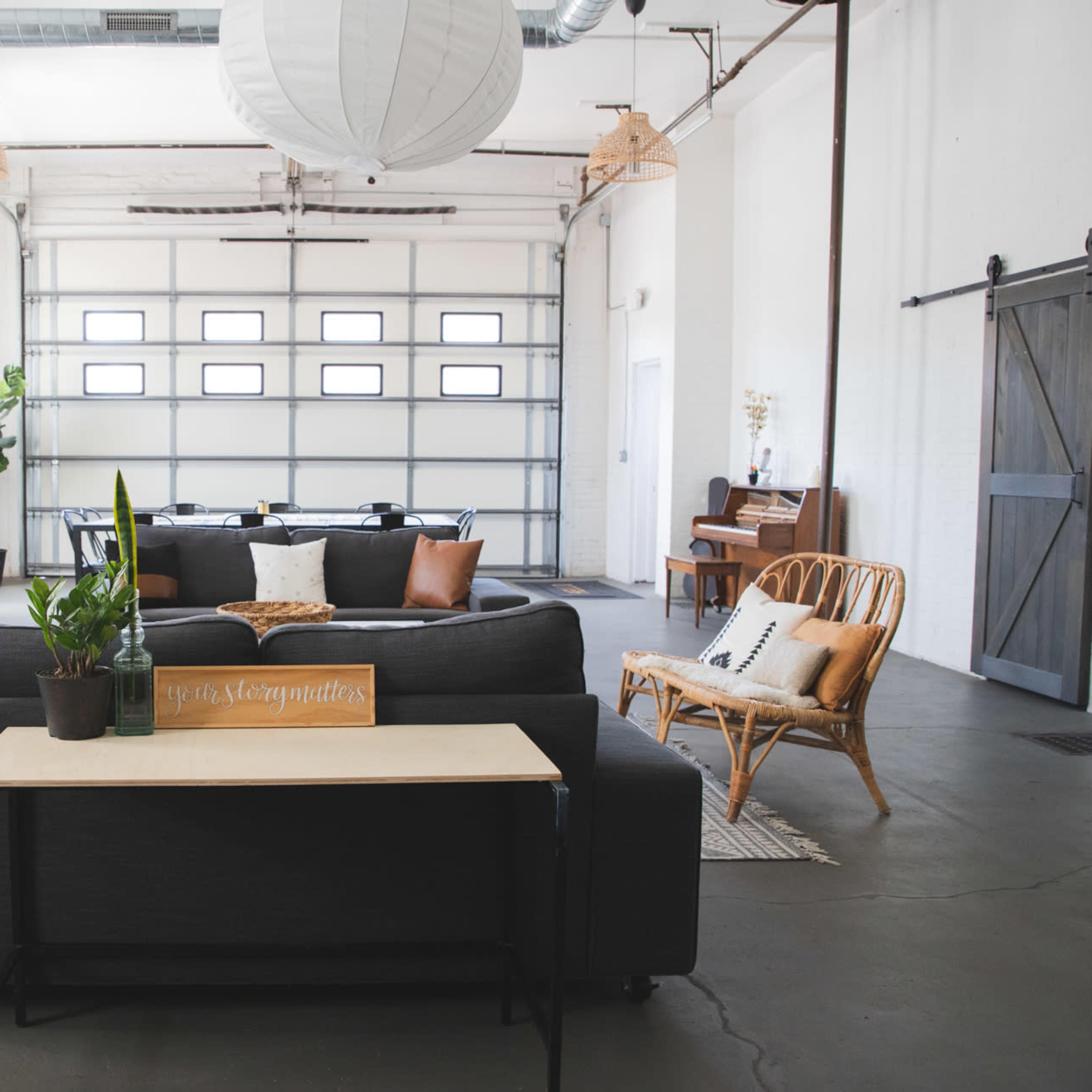 A spacious, minimalist living area with modern furniture, a large garage door, and a piano in the background.
