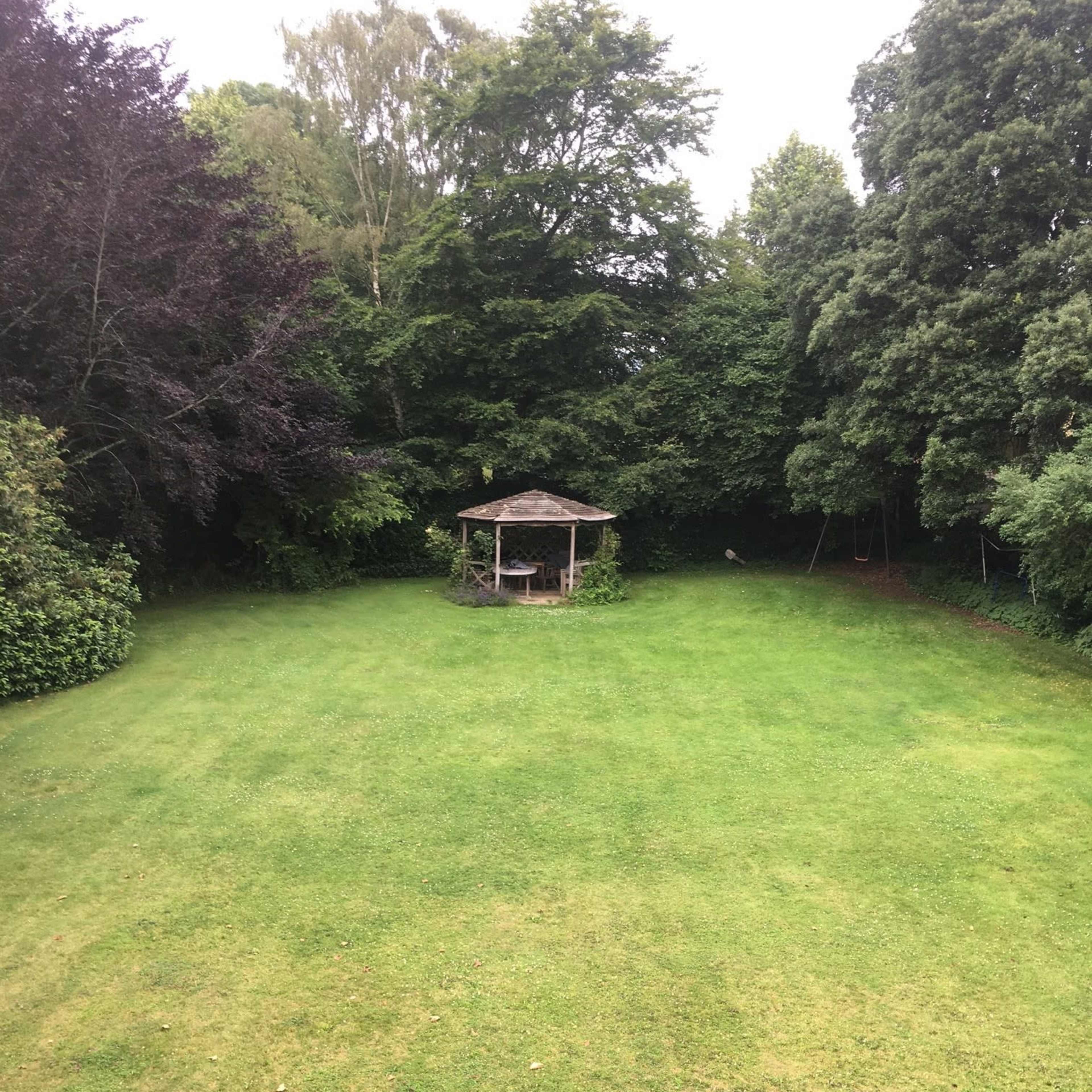 A spacious green lawn with a gazebo surrounded by trees in the background.