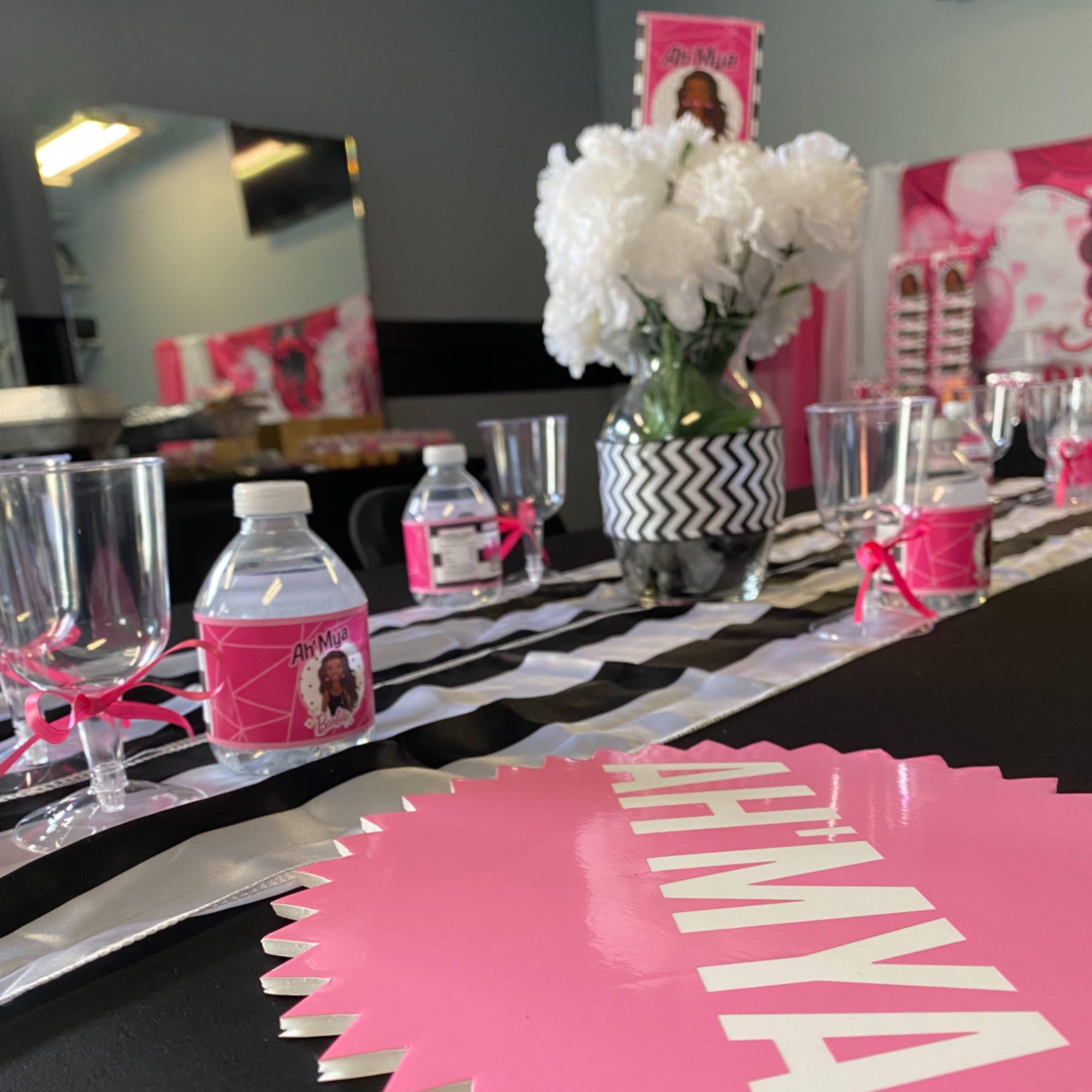 A decorated table set with a black tablecloth, pink and silver accents, clear glasses, water bottles, and a floral centerpiece.