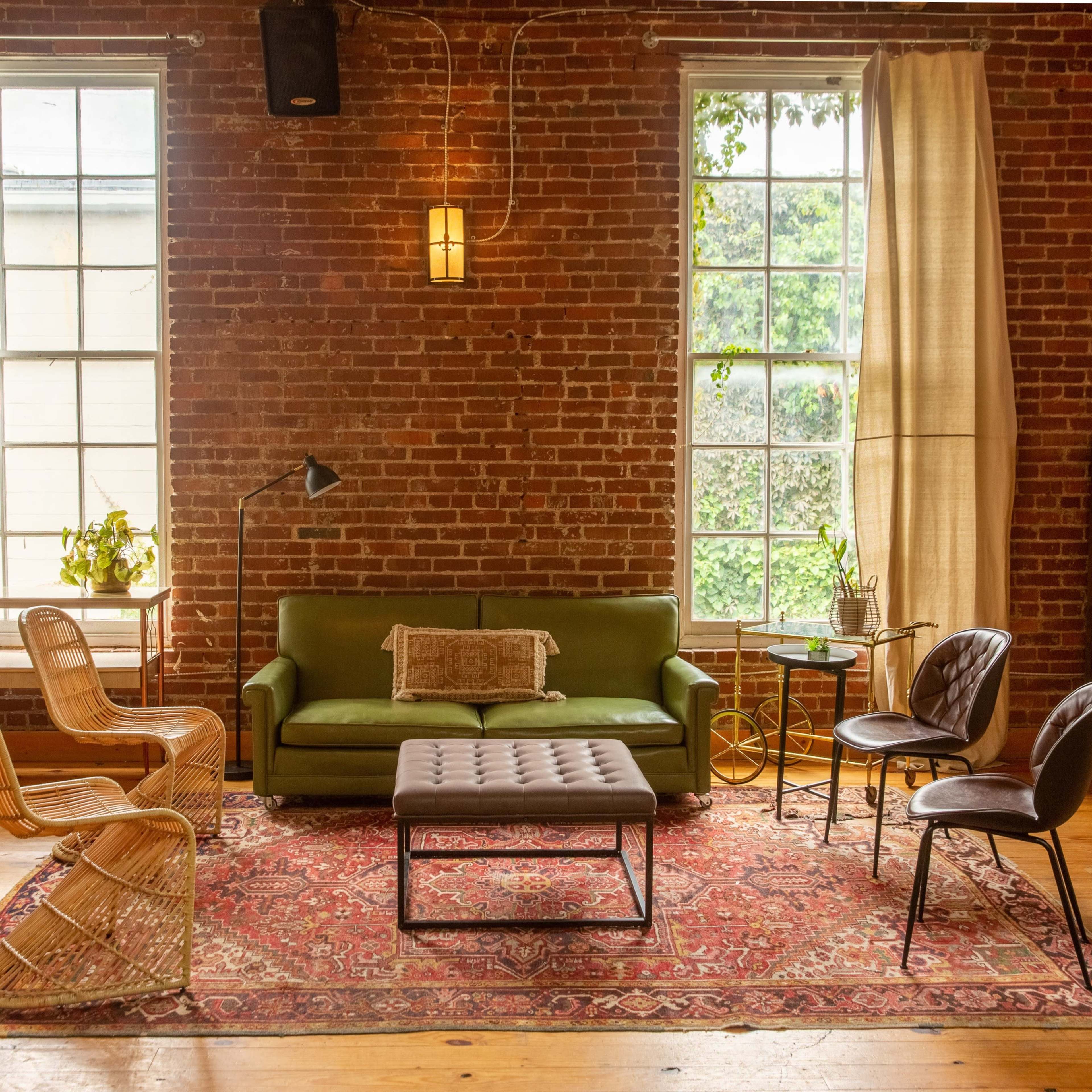 A cozy living room with exposed brick walls, a green couch, a coffee table, and various seating options arranged around a patterned rug.