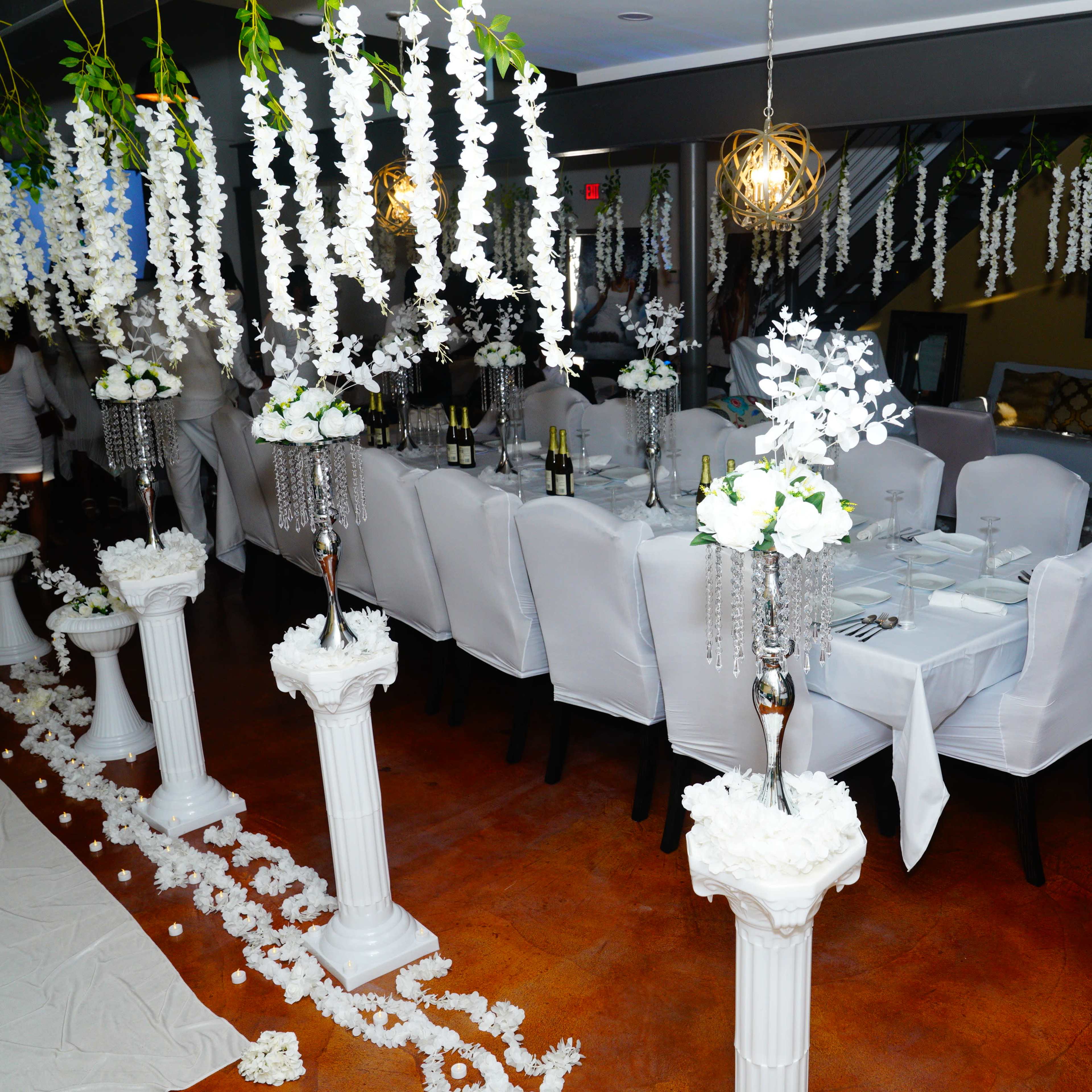 A elegantly decorated dining space with white-clothed tables set for an event, surrounded by floral arrangements and hanging decorations.