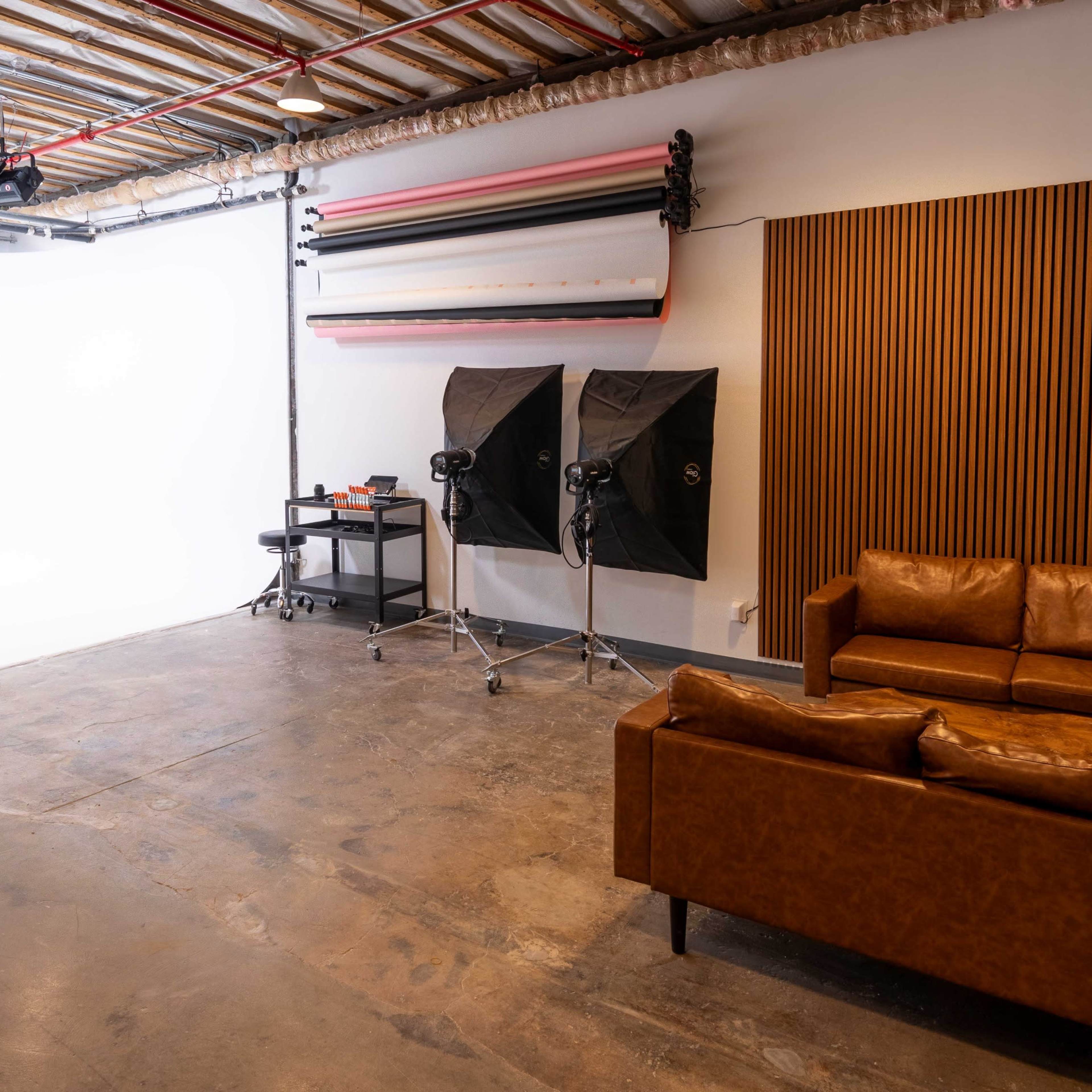 A photography studio featuring a white backdrop, studio lights, and a leather sofa against a wooden wall.