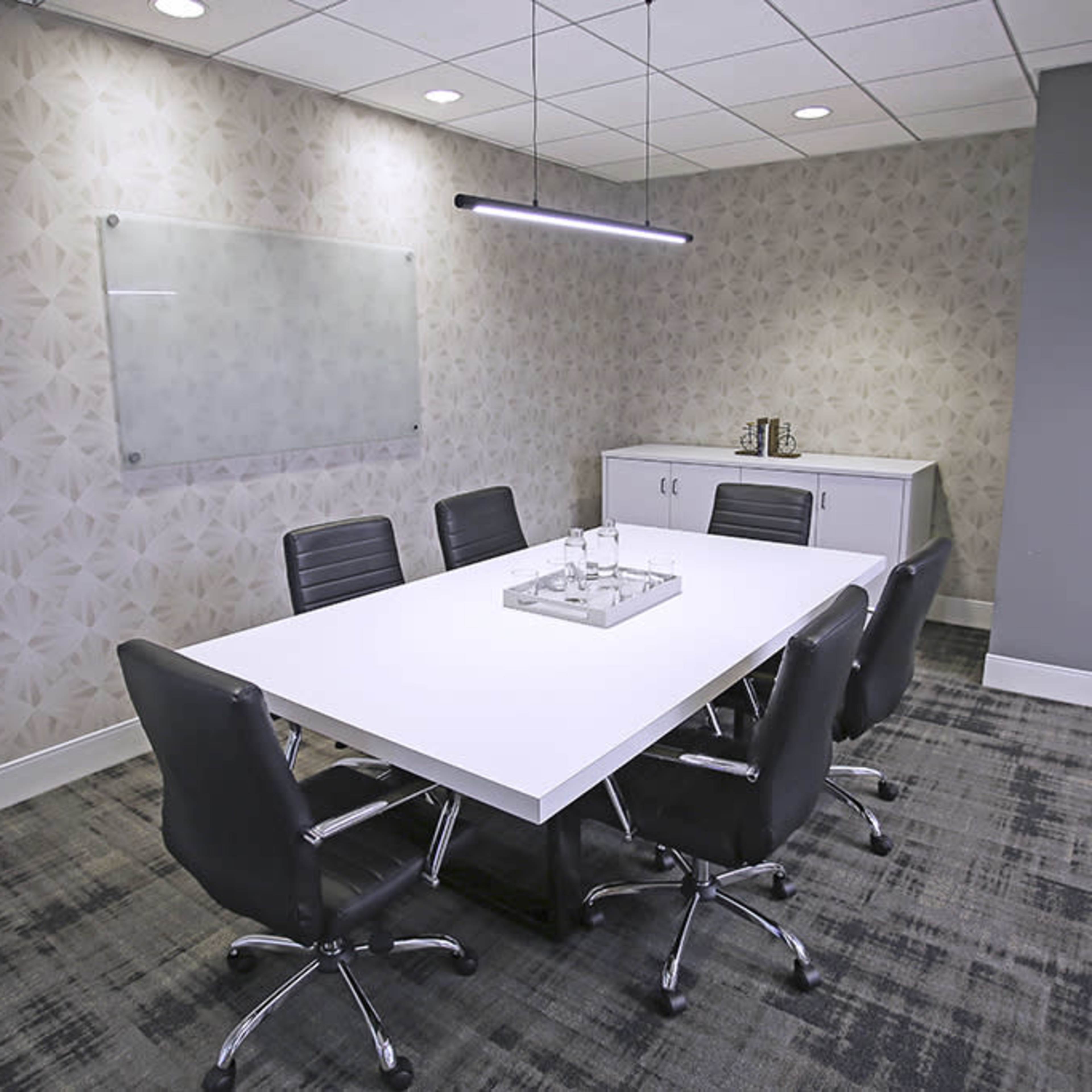 A modern conference room features a large white table surrounded by black chairs, with a minimalist design and a side cabinet.