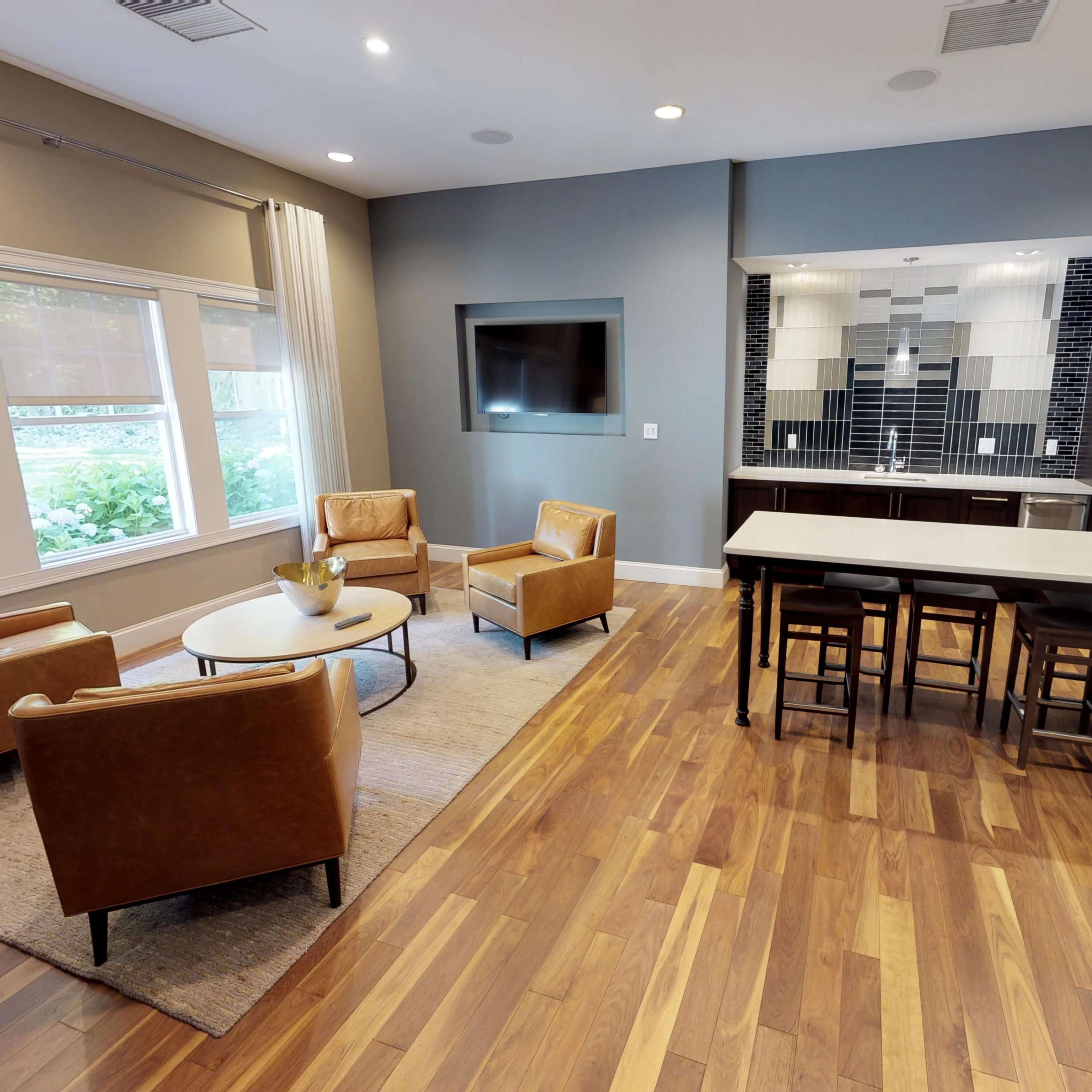 A modern living space with a seating area featuring two armchairs and a coffee table, alongside a kitchen with barstools and sleek appliances.