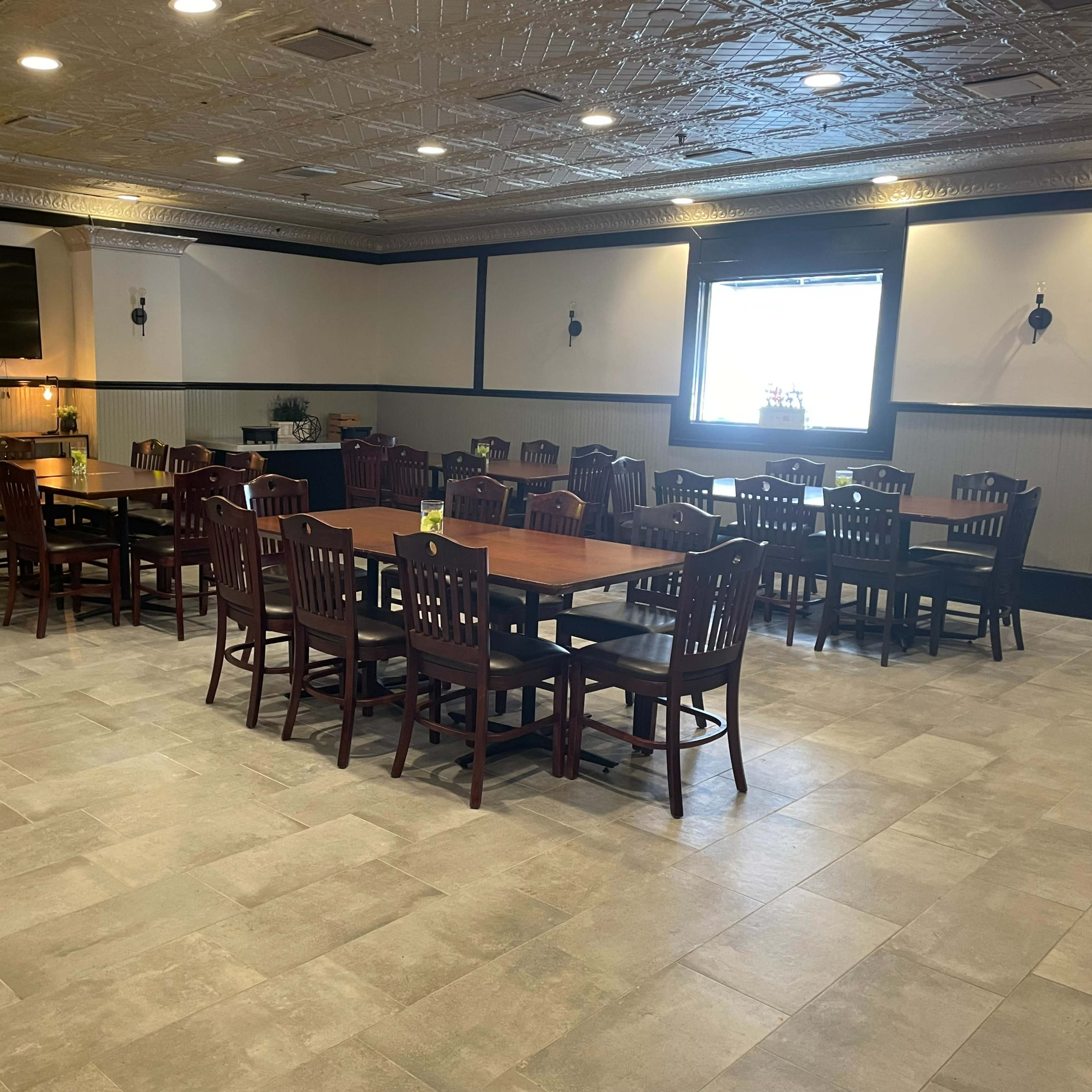 A spacious dining area features rows of wooden tables and chairs, with a large TV mounted on the wall.