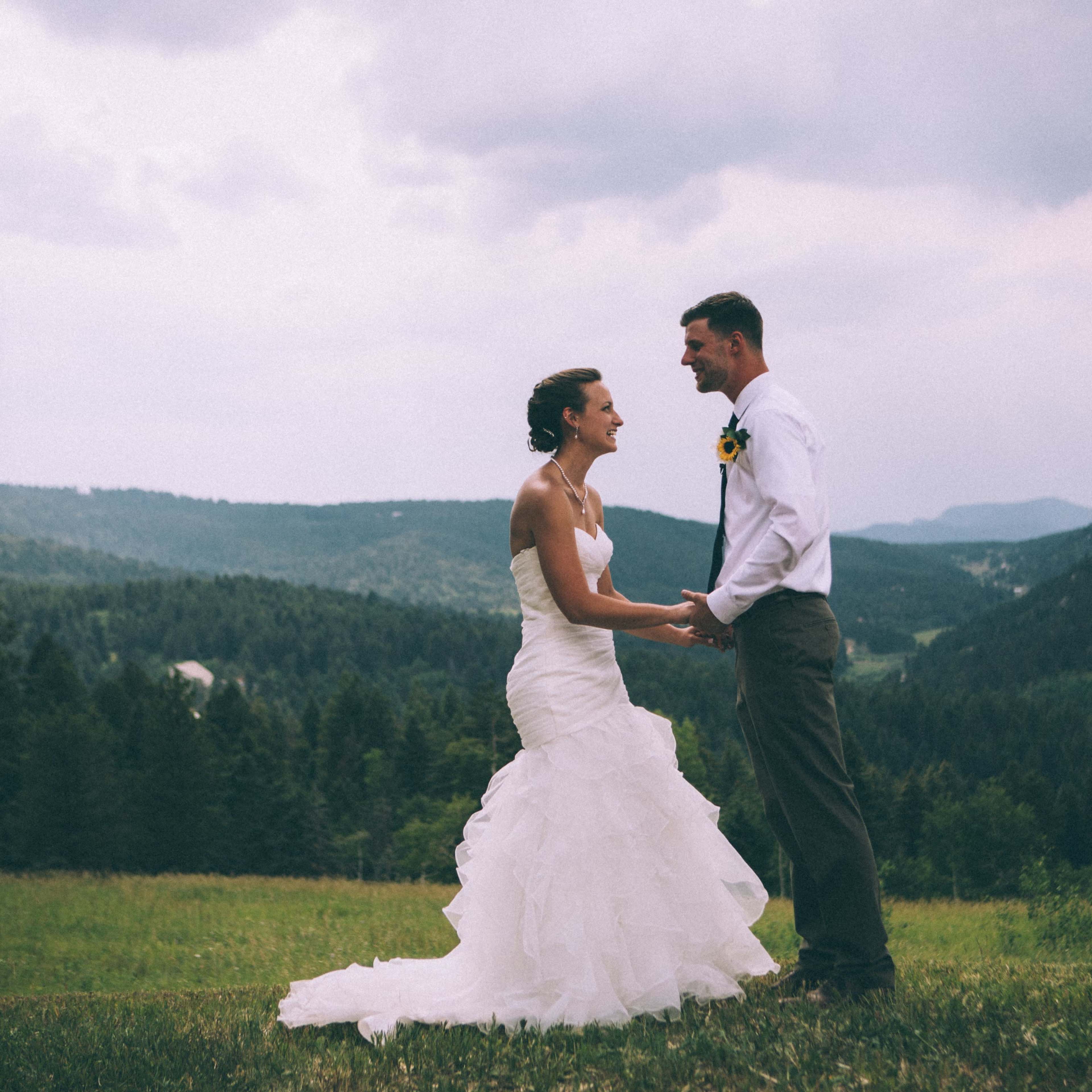 A bride and groom hold hands during their outdoor wedding ceremony in a mountainous landscape.