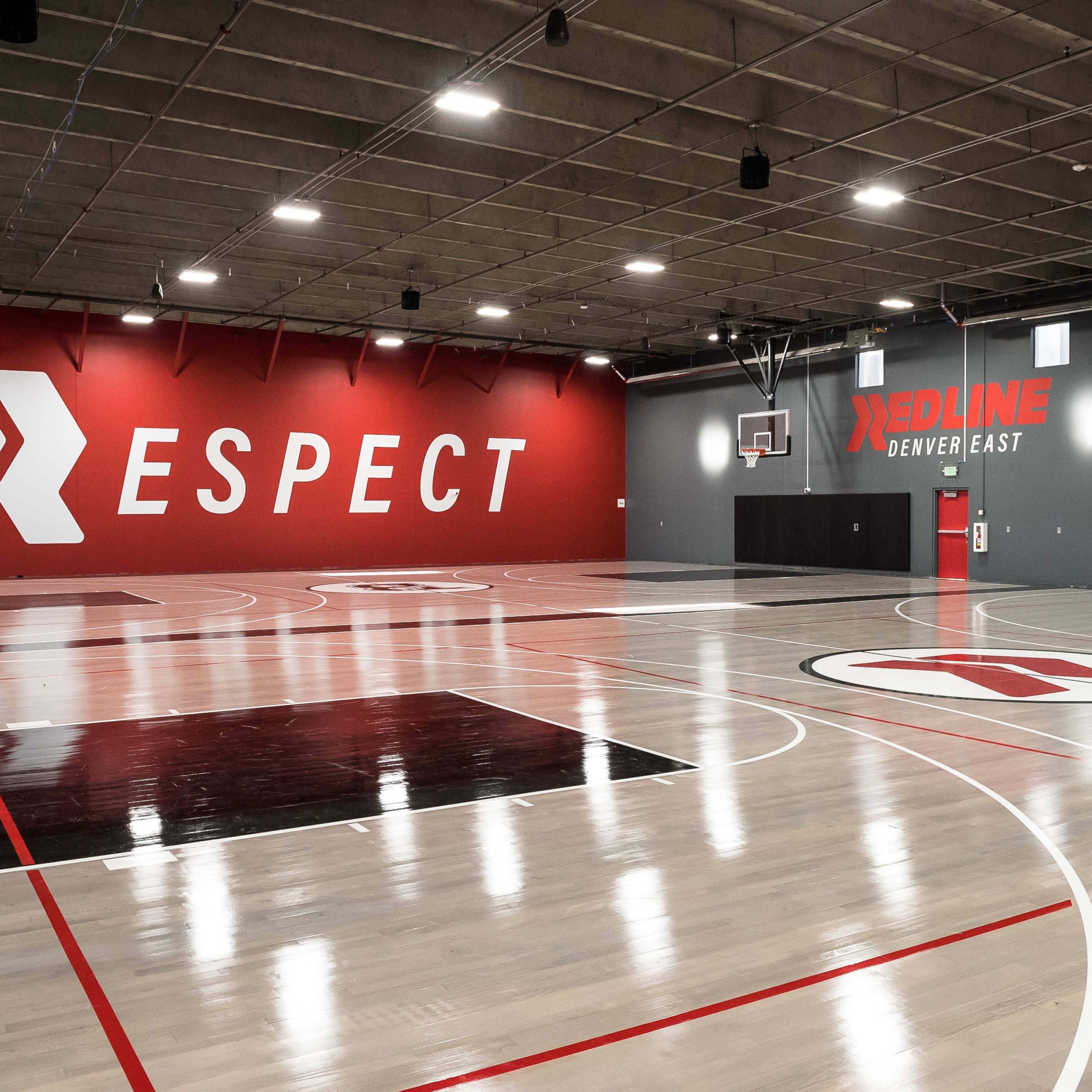 An indoor basketball court with a red wall featuring the word "RESPECT" and a gray wall with the logo "REDLINE DENVER EAST."