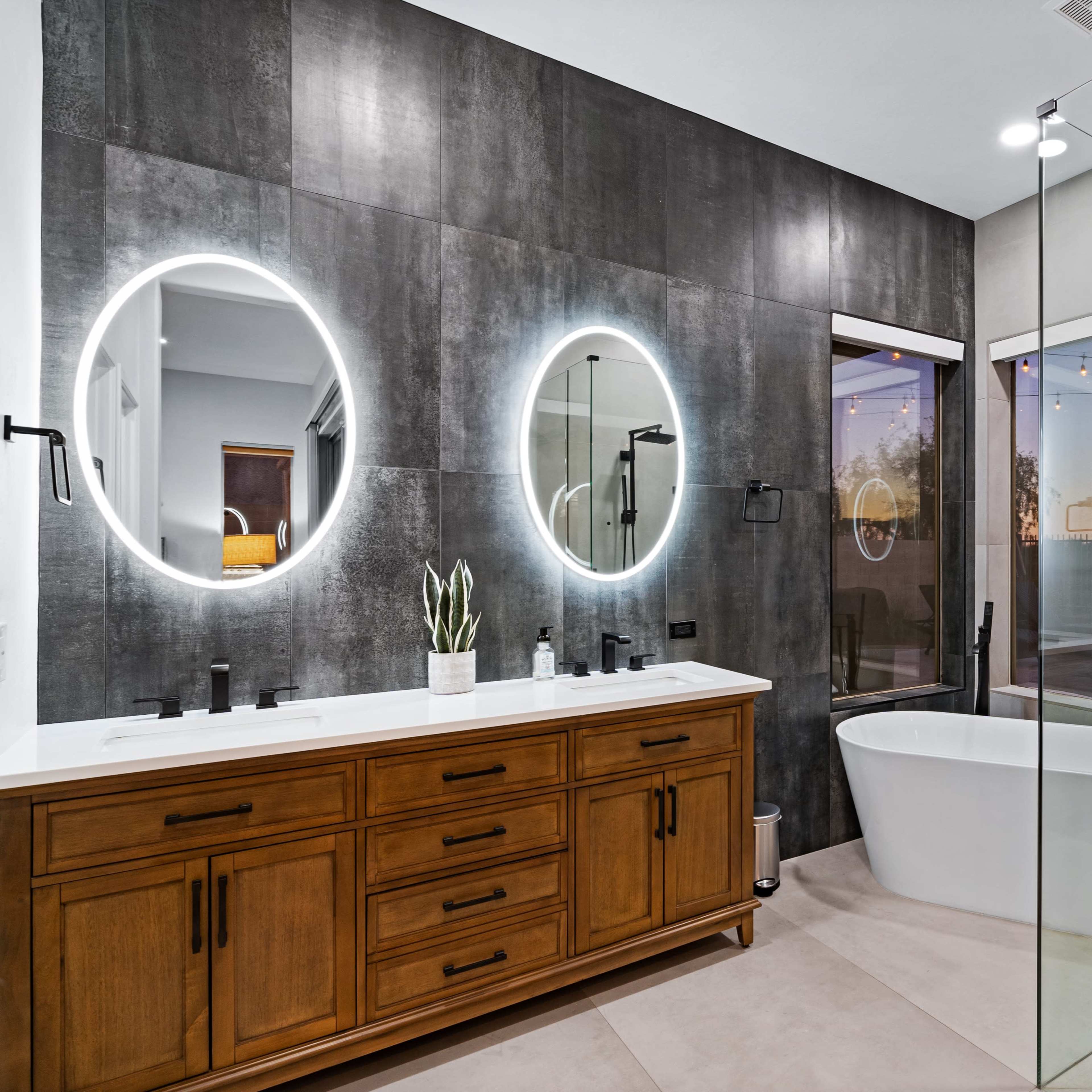 A modern bathroom featuring a double vanity with circular mirrors, a freestanding bathtub, and a glass shower enclosure.