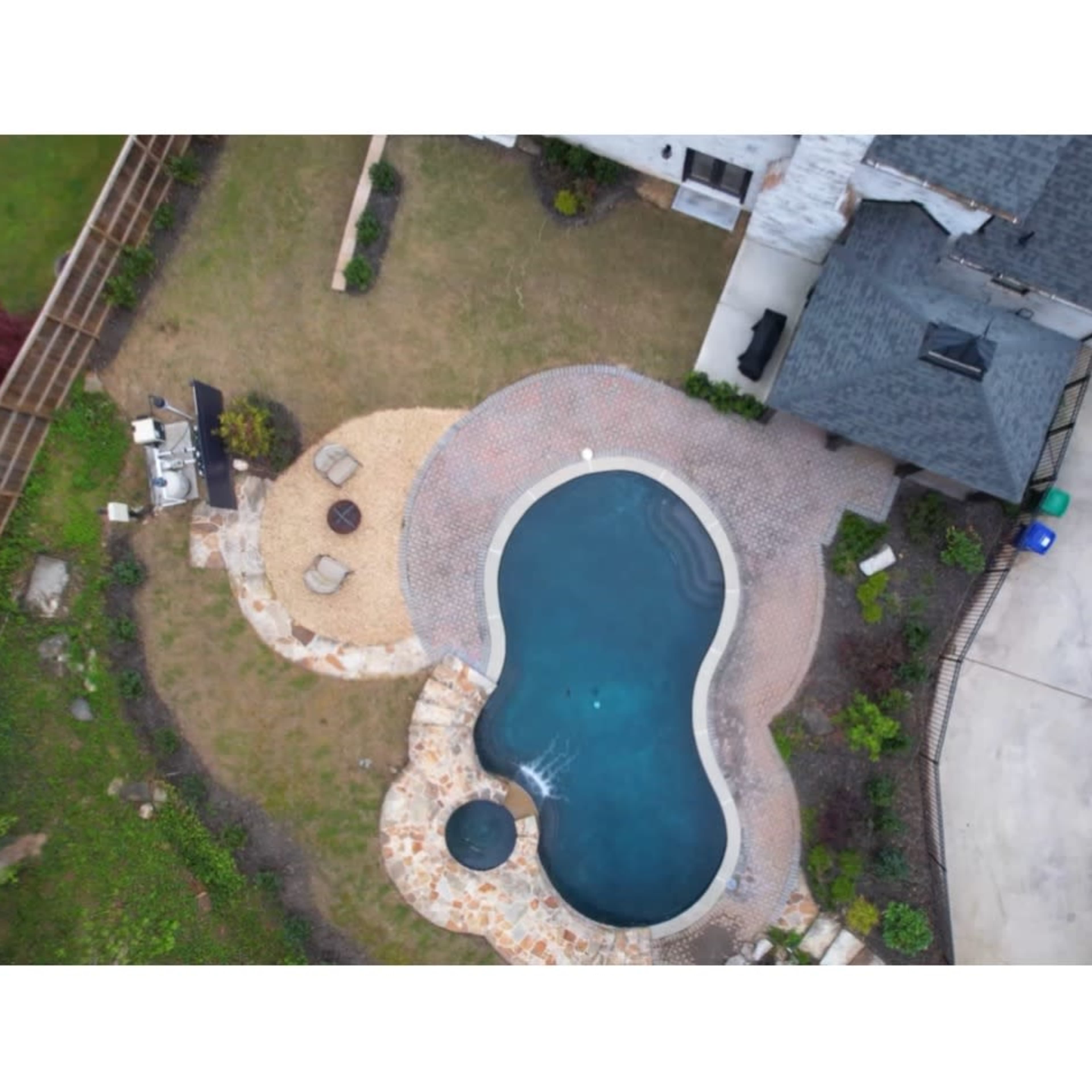 An aerial view of a landscaped backyard featuring a kidney-shaped pool surrounded by stone pathways and seating areas.