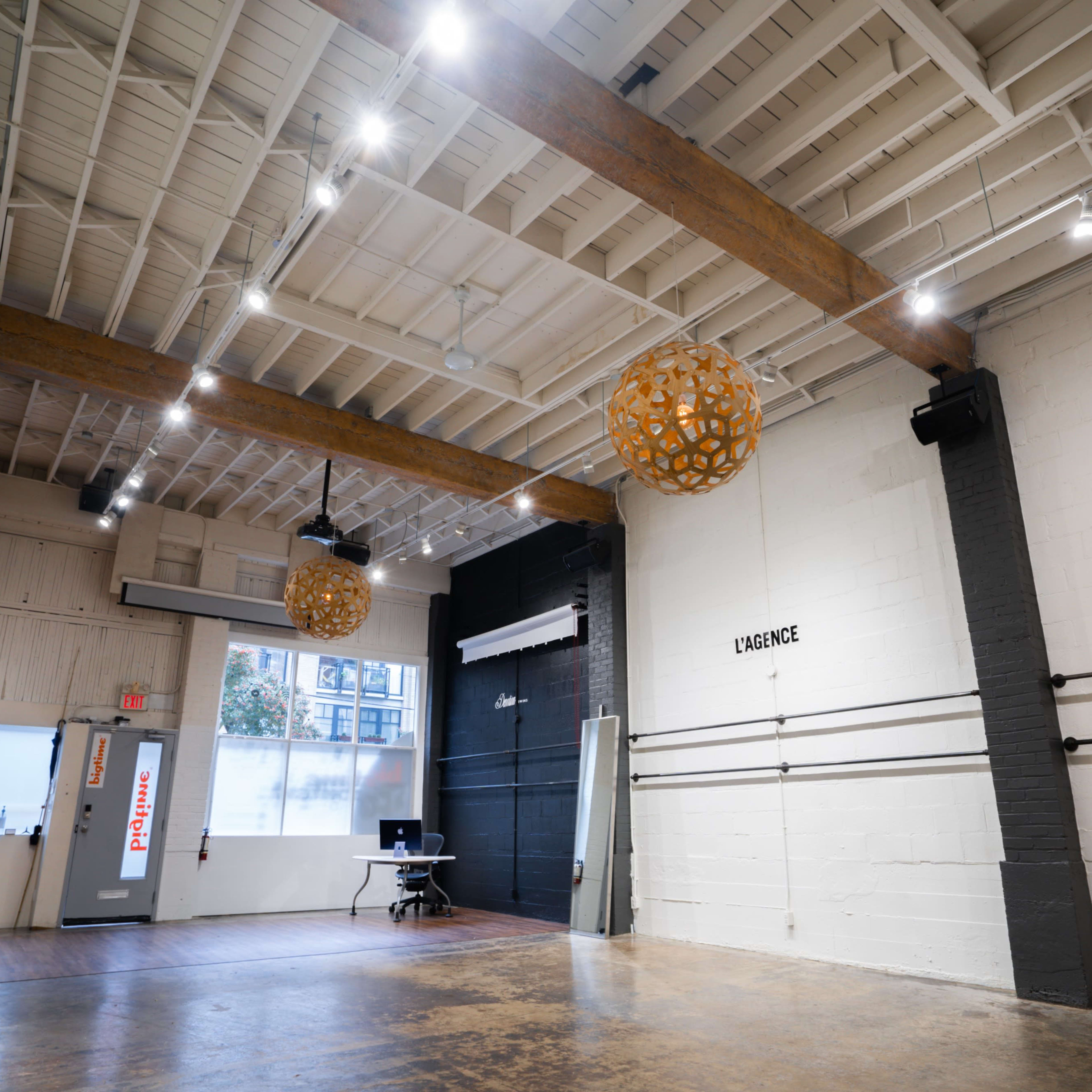A spacious, well-lit studio with wooden beams, two large decorative lanterns hanging from the ceiling, and a black wall with the word "KANGOL" displayed.