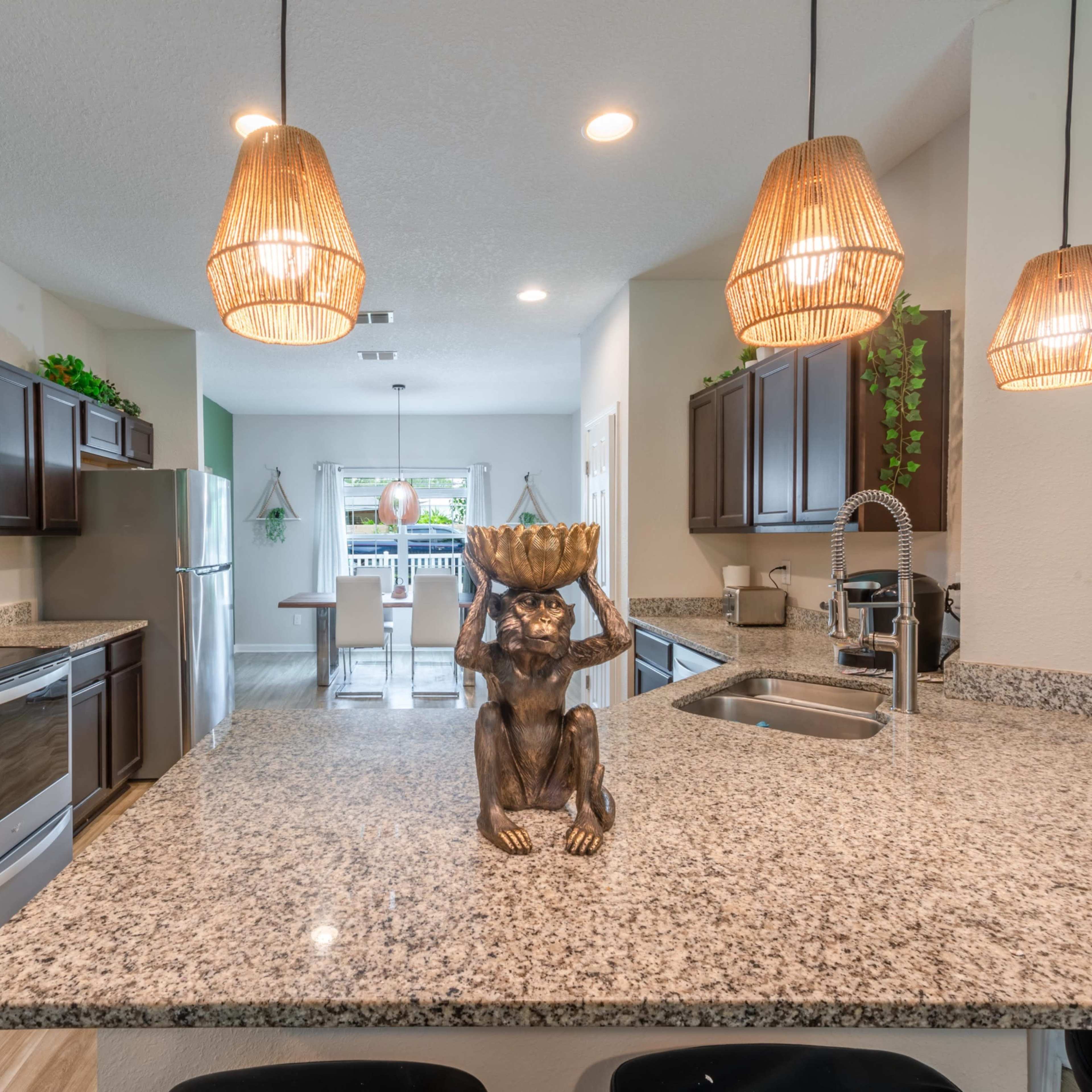 A modern kitchen features dark wood cabinets, stainless steel appliances, and a large granite island with decorative items and pendant lighting.